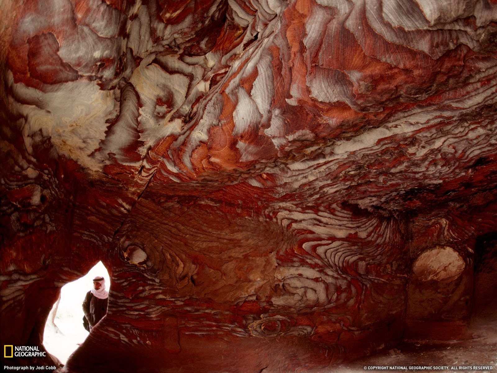 Cave interior with colorful rock formations and a person HD Wallpaper