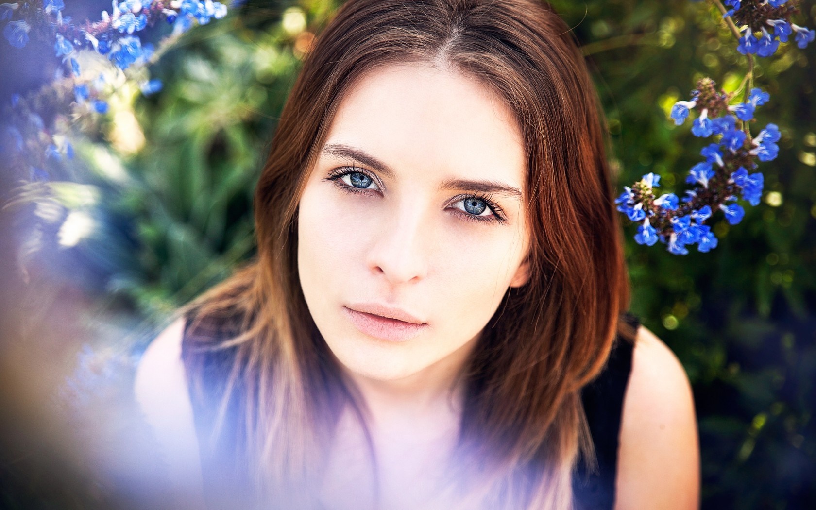 Woman with blue eyes and brown hair outdoors with blue flowers HD Wallpaper