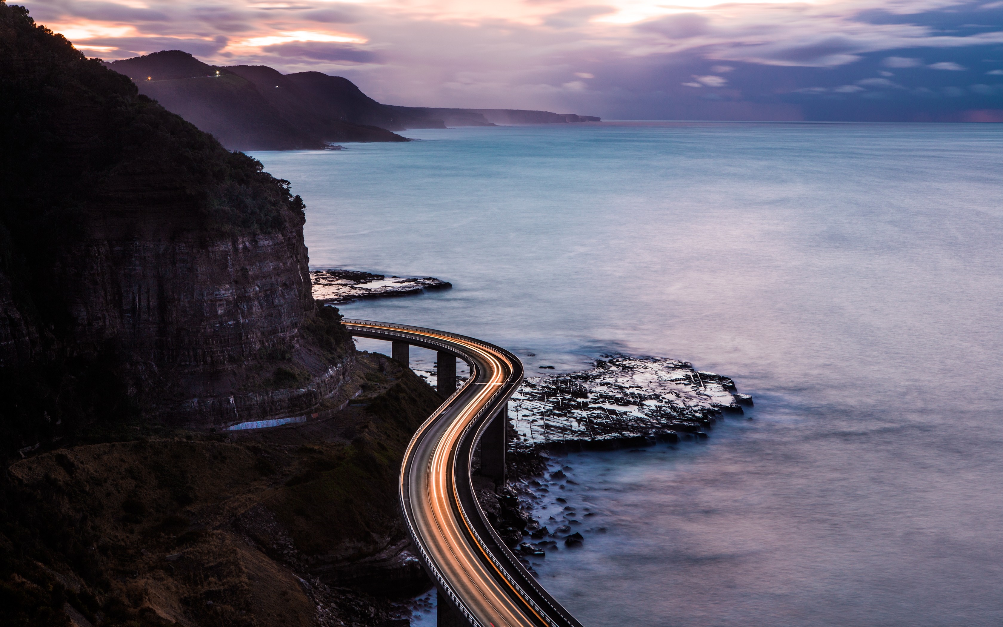 Coastal road with light trails at dusk HD Wallpaper