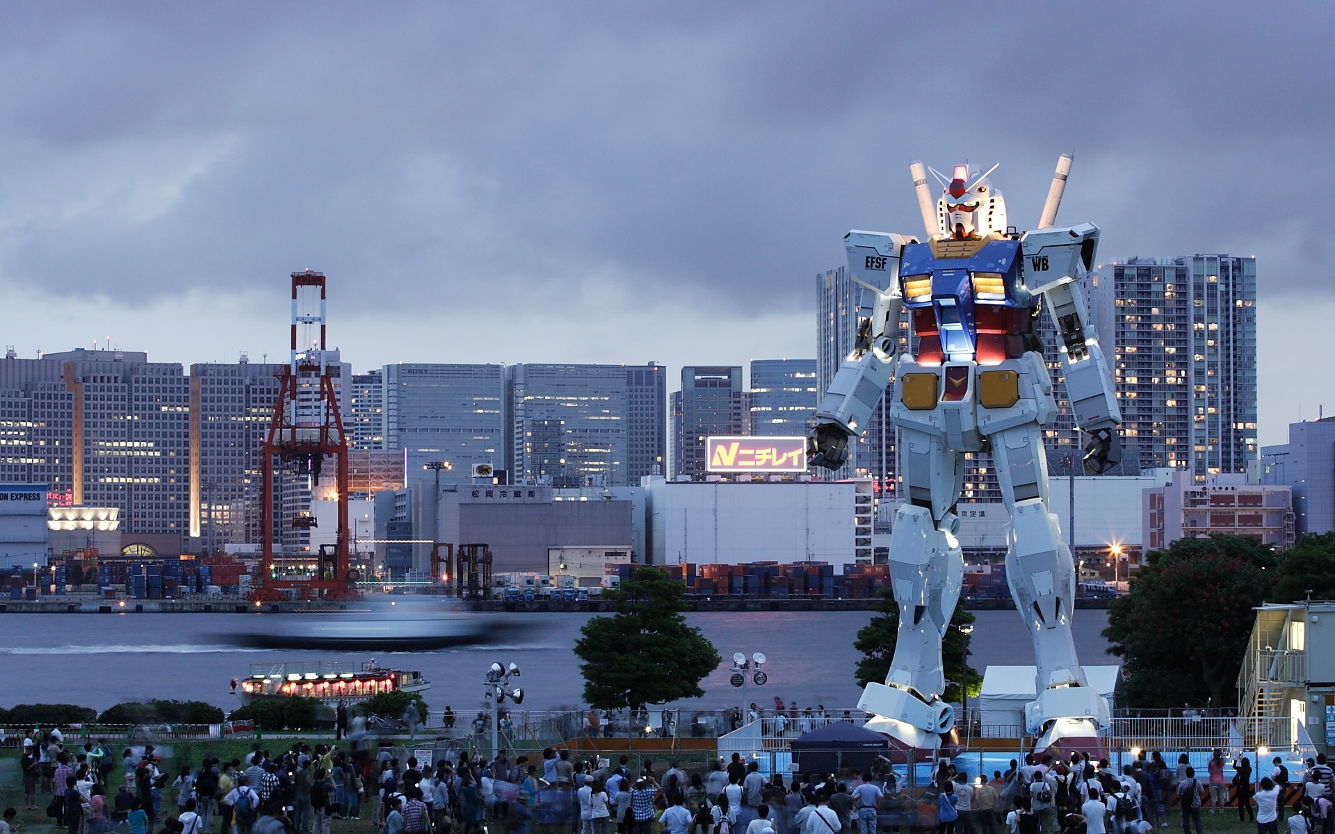Giant Gundam statue in a city harbor at dusk HD Wallpaper