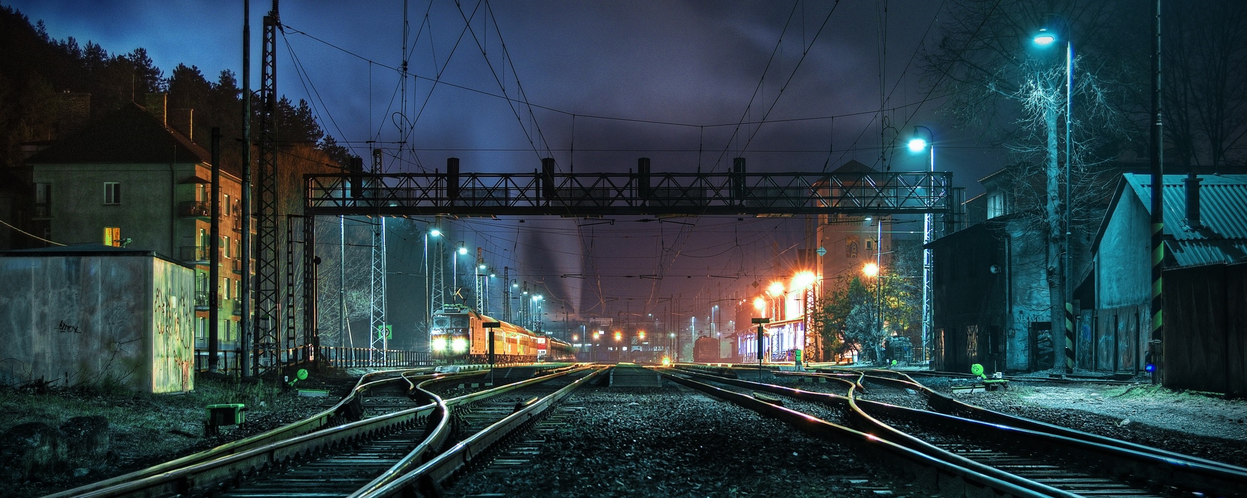 Train station at night with illuminated train and tracks HD Wallpaper
