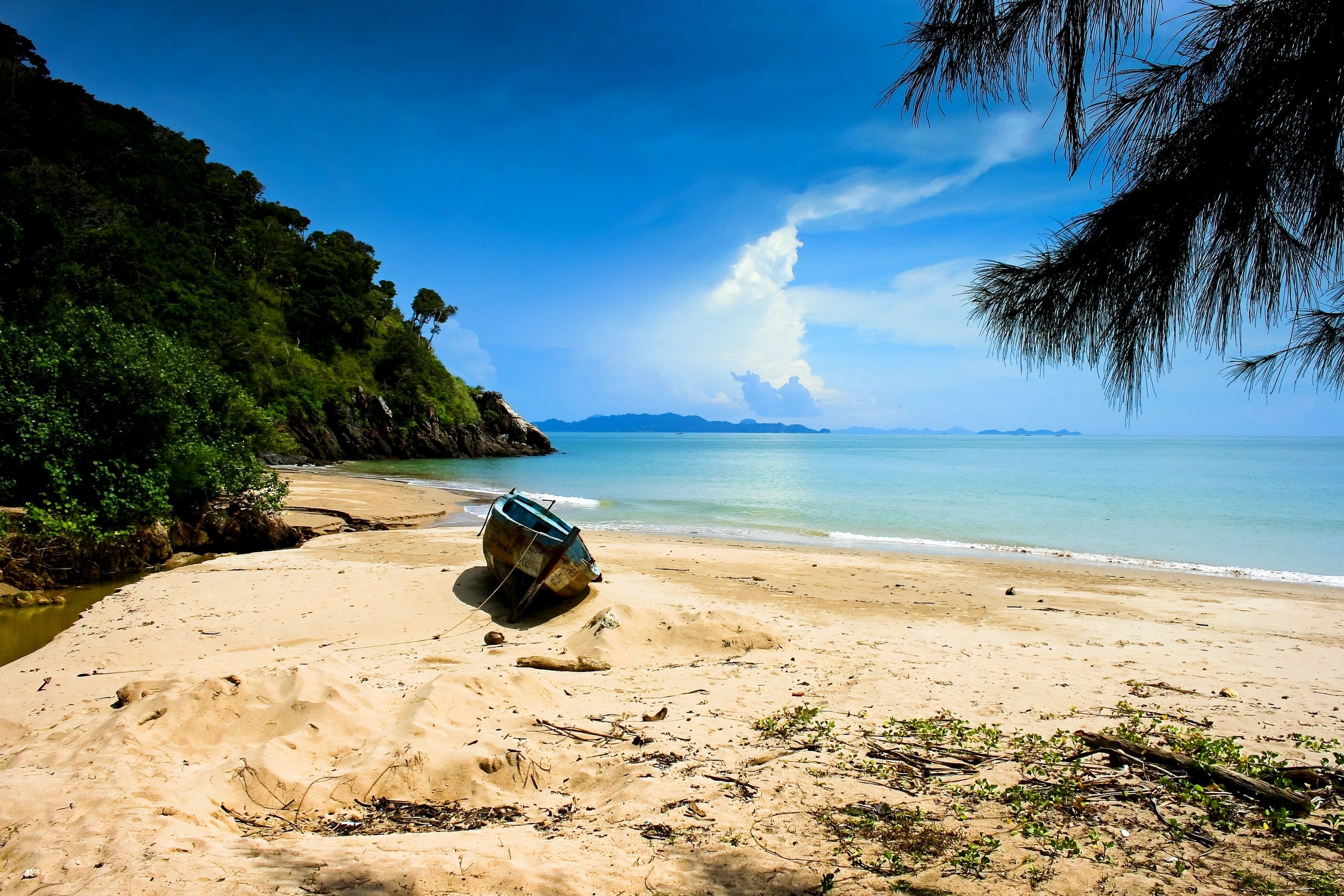 Boat on a sandy beach with a lush green hill and blue ocean HD Wallpaper