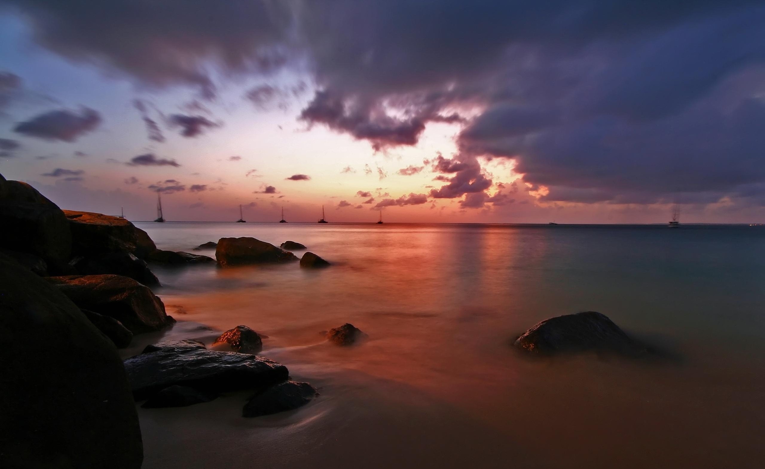 Sunset over the ocean with sailboats and rocks HD Wallpaper