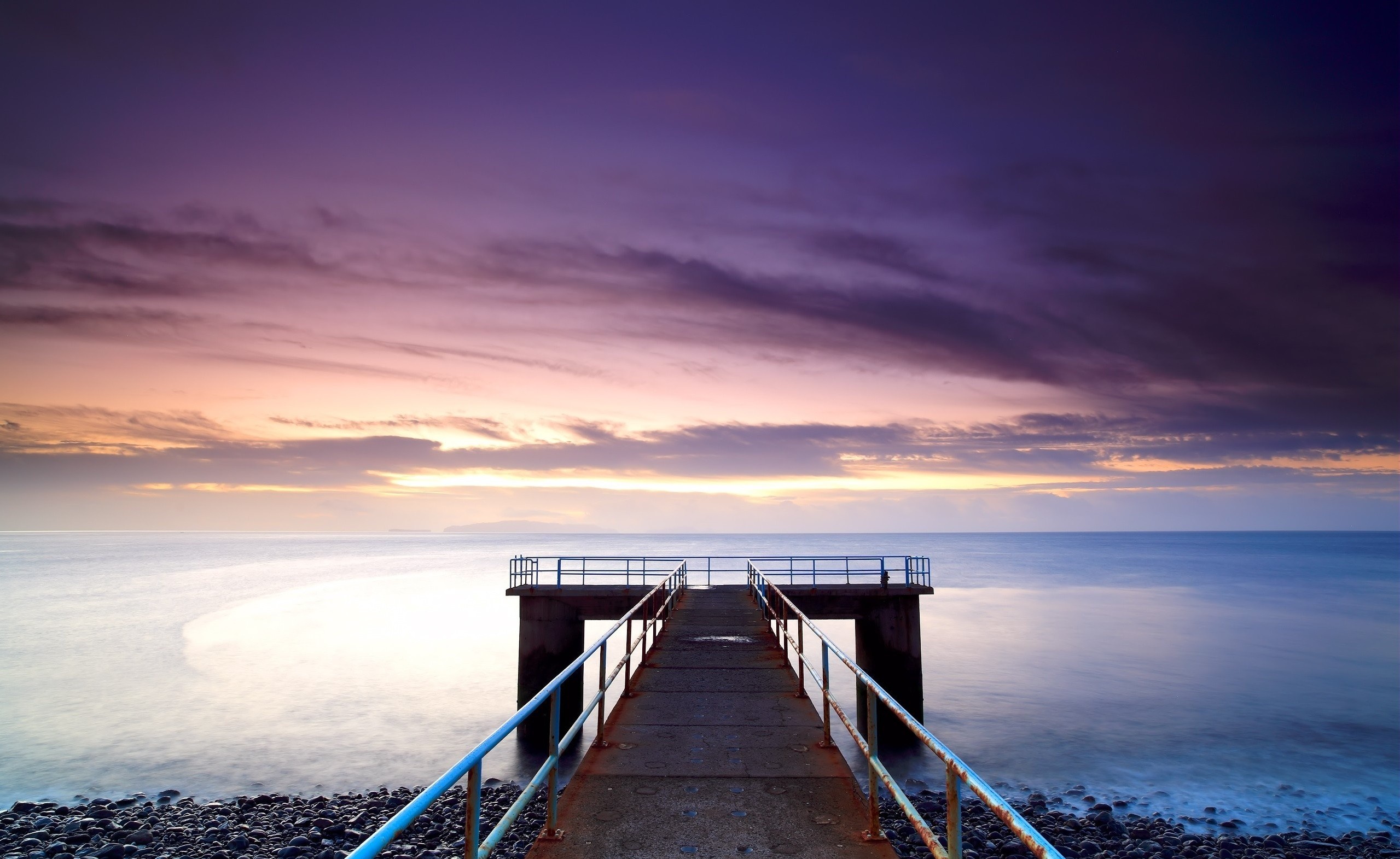 Pier extending into the ocean at sunset with purple clouds HD Wallpaper