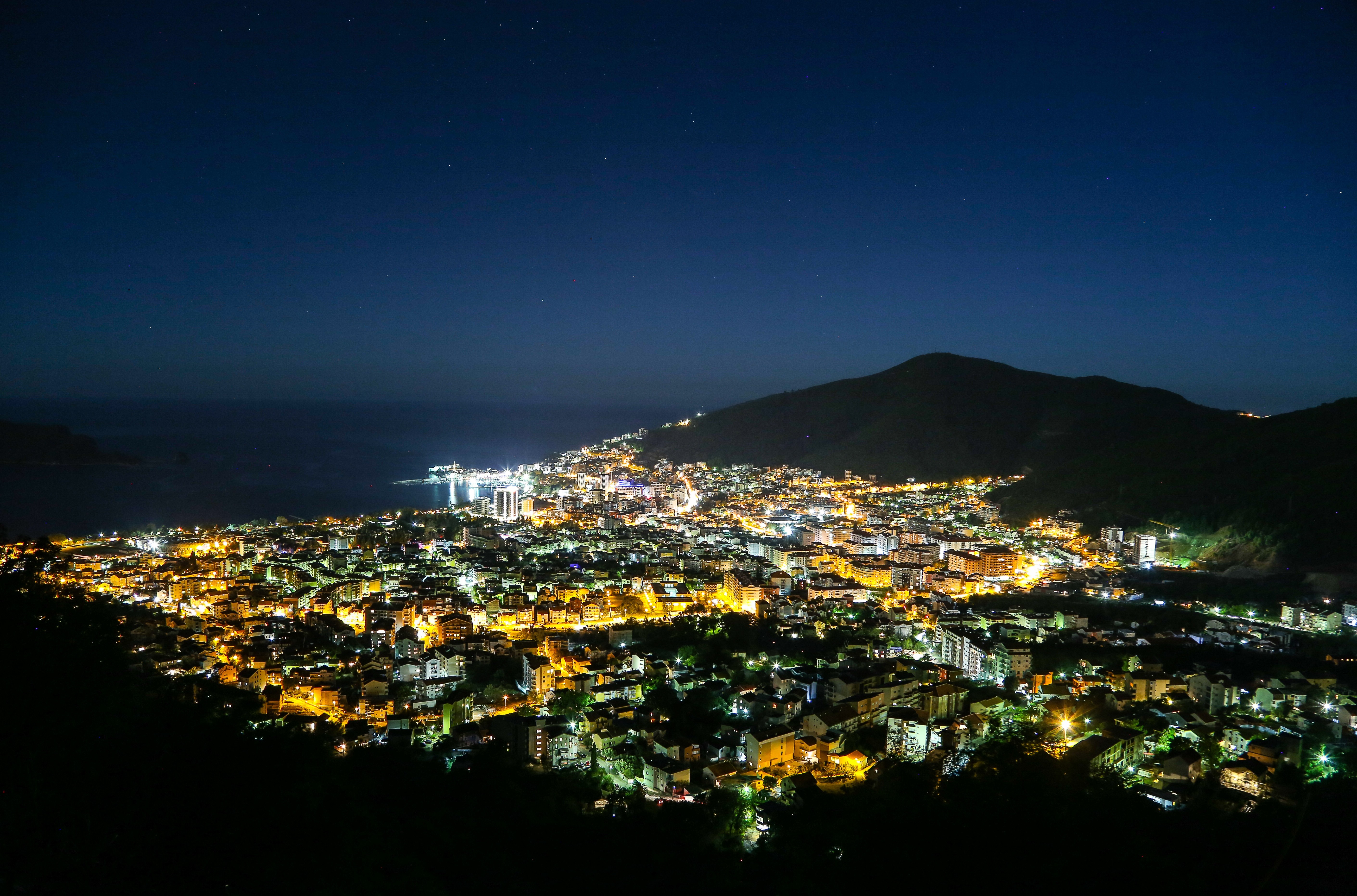 Cityscape at night with mountains and sea HD Wallpaper