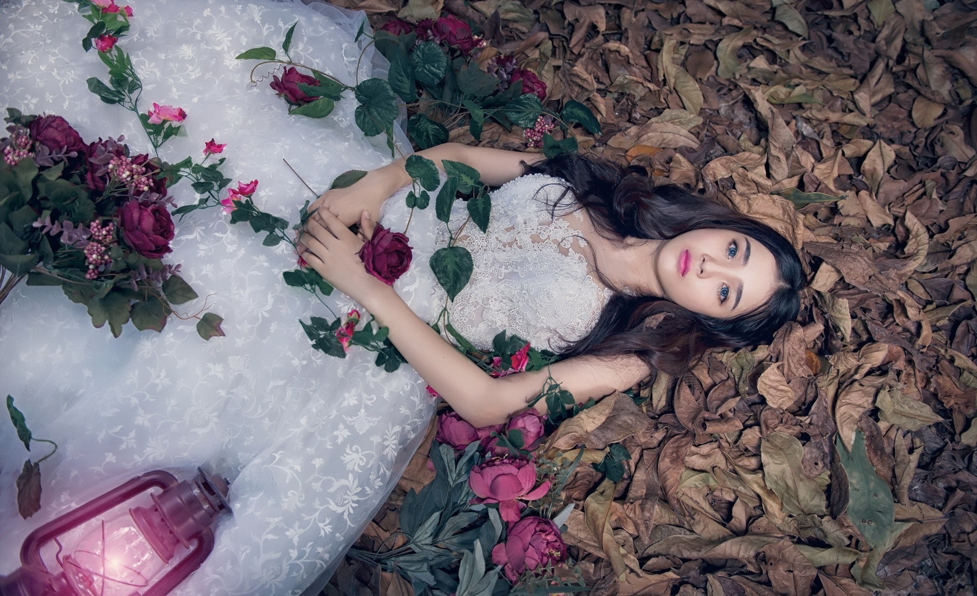 Woman in white dress lying among leaves and flowers with a lantern HD Wallpaper