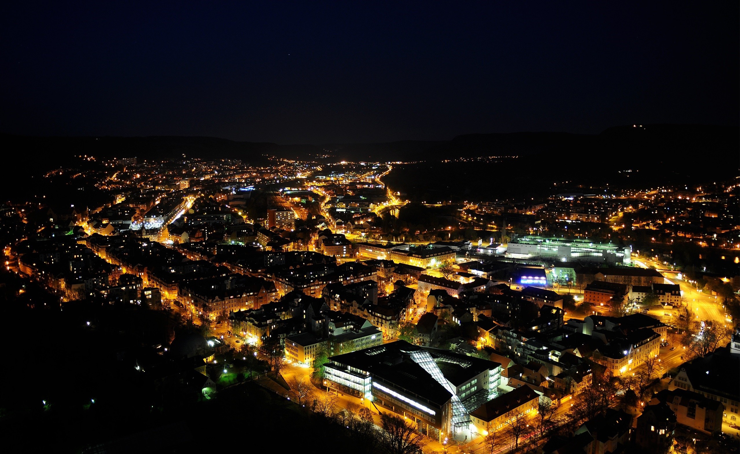 Aerial view of a city at night with illuminated buildings HD Wallpaper
