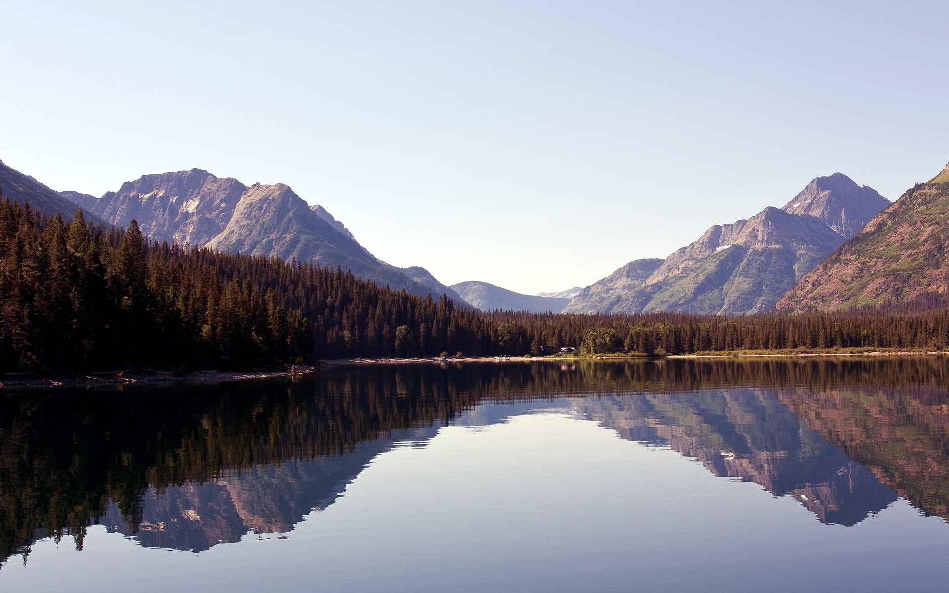 Mountain range reflected in a calm lake with pine forest HD Wallpaper