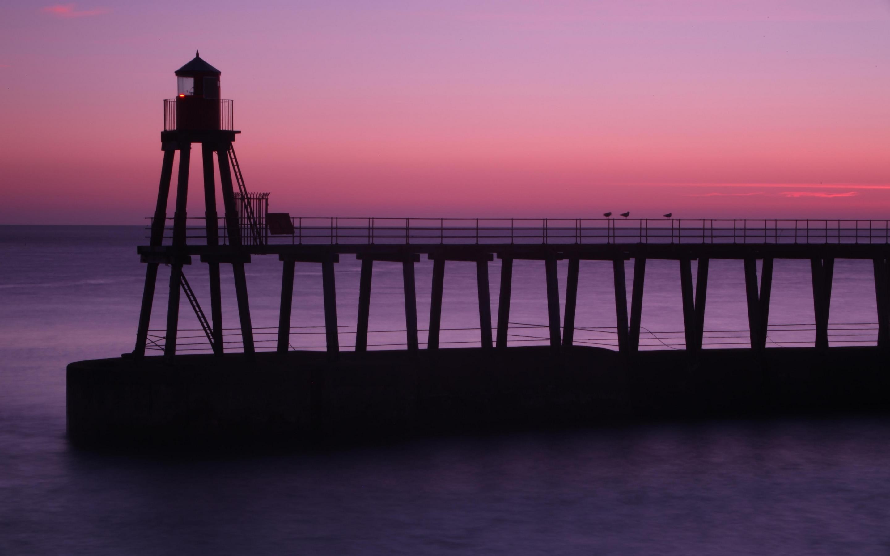 Silhouette of a lighthouse and pier at sunset over the sea HD Wallpaper