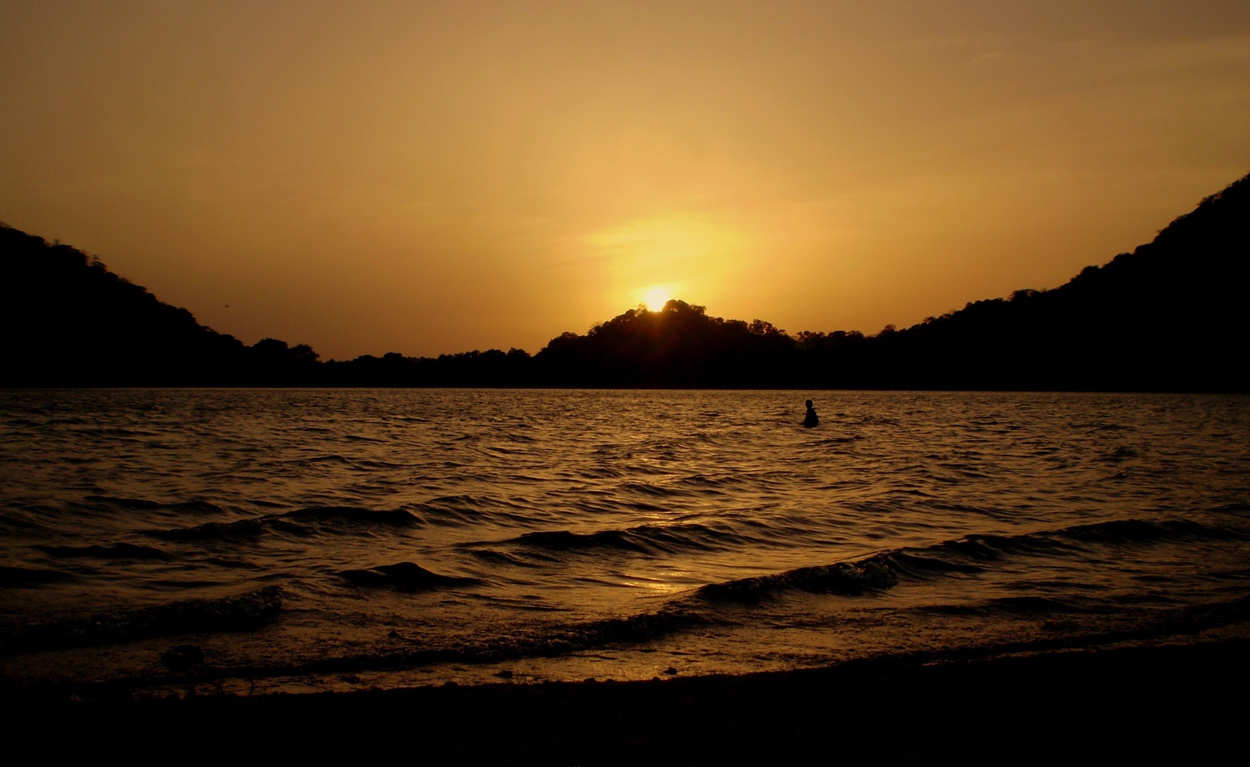 Sunset over a body of water with a person swimming HD Wallpaper