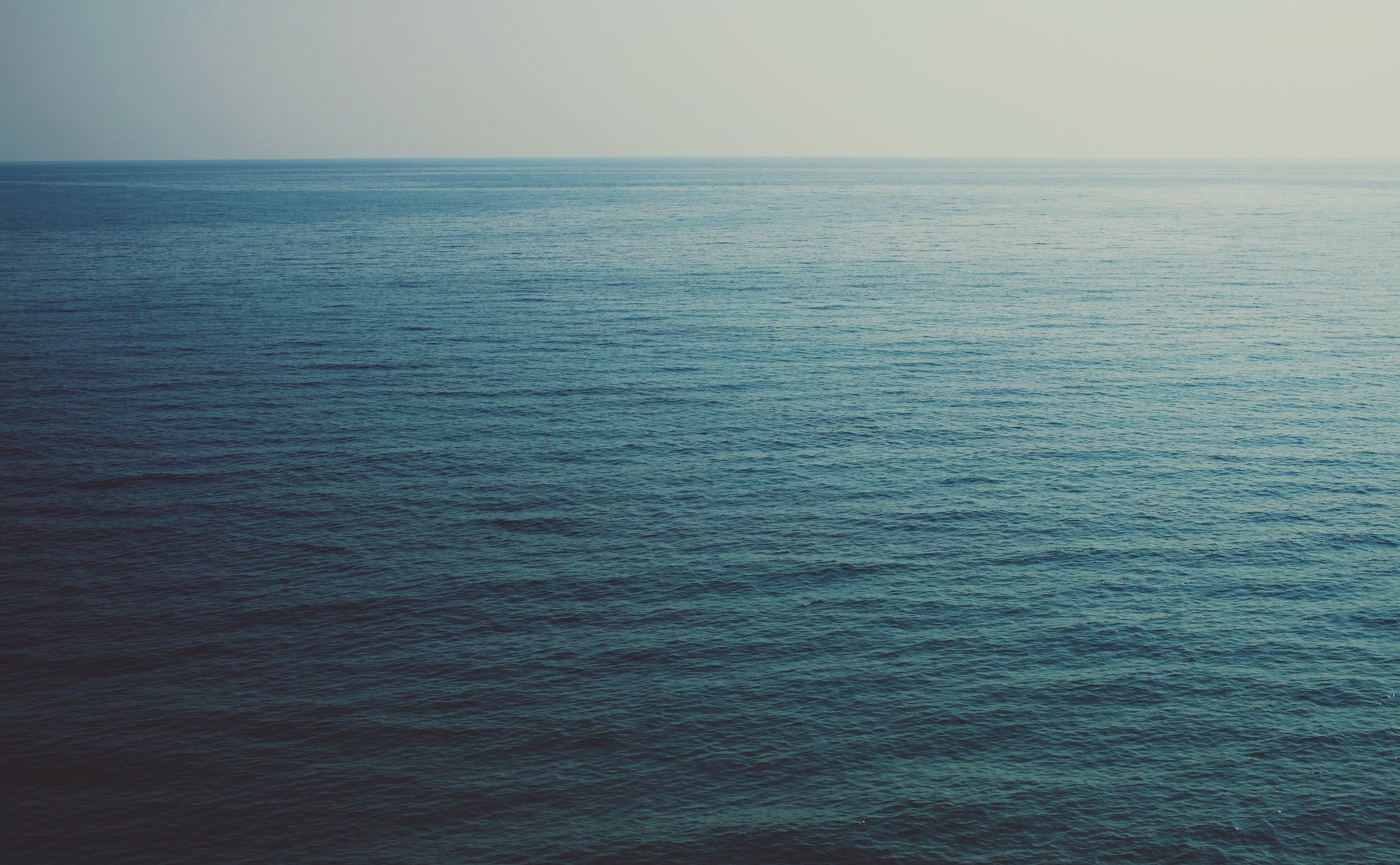 Ocean horizon with gentle waves under a pale sky HD Wallpaper