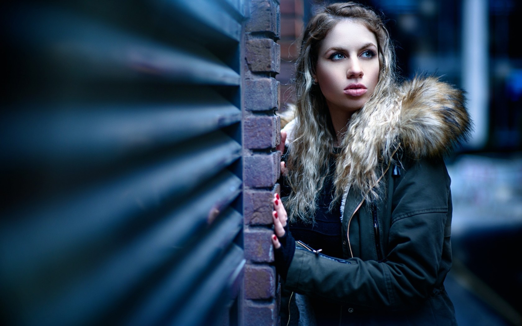 Woman in fur-lined jacket leaning against a brick wall HD Wallpaper