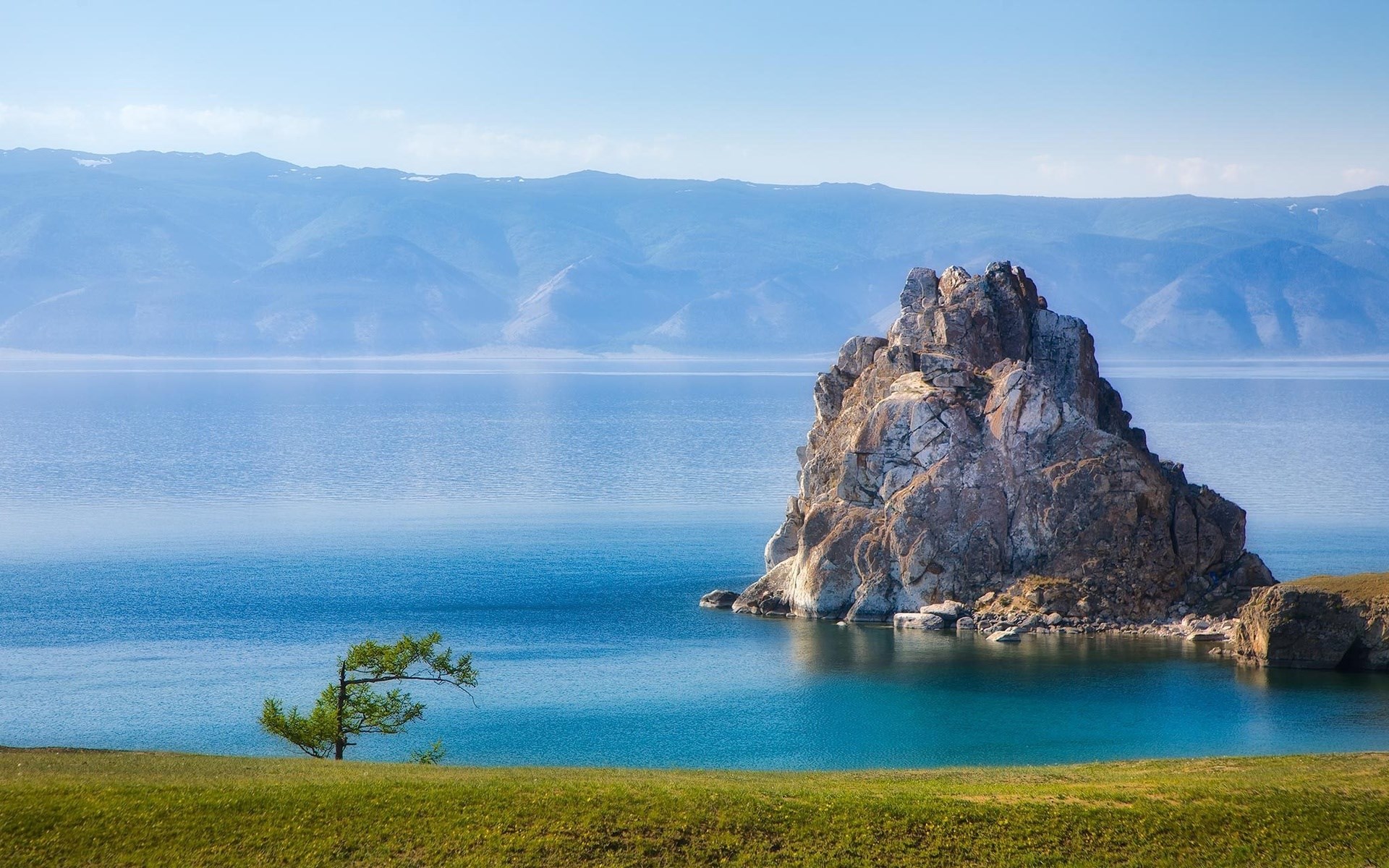 Rock formation in a lake with mountains in the background HD Wallpaper
