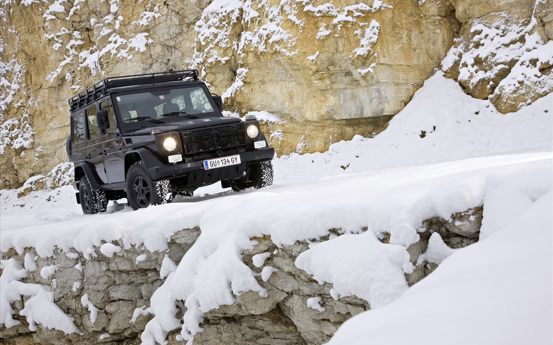 Black Mercedes-Benz G-Wagon driving on a snowy mountain road HD Wallpaper