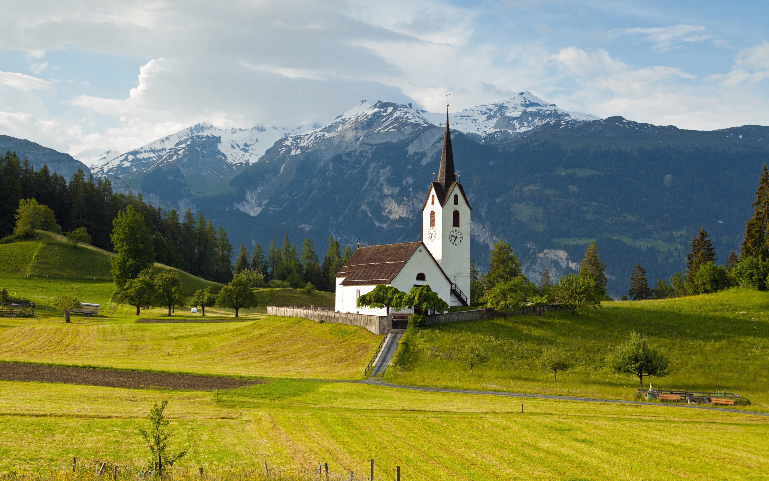 White church on a grassy hill with snow-capped mountains HD Wallpaper
