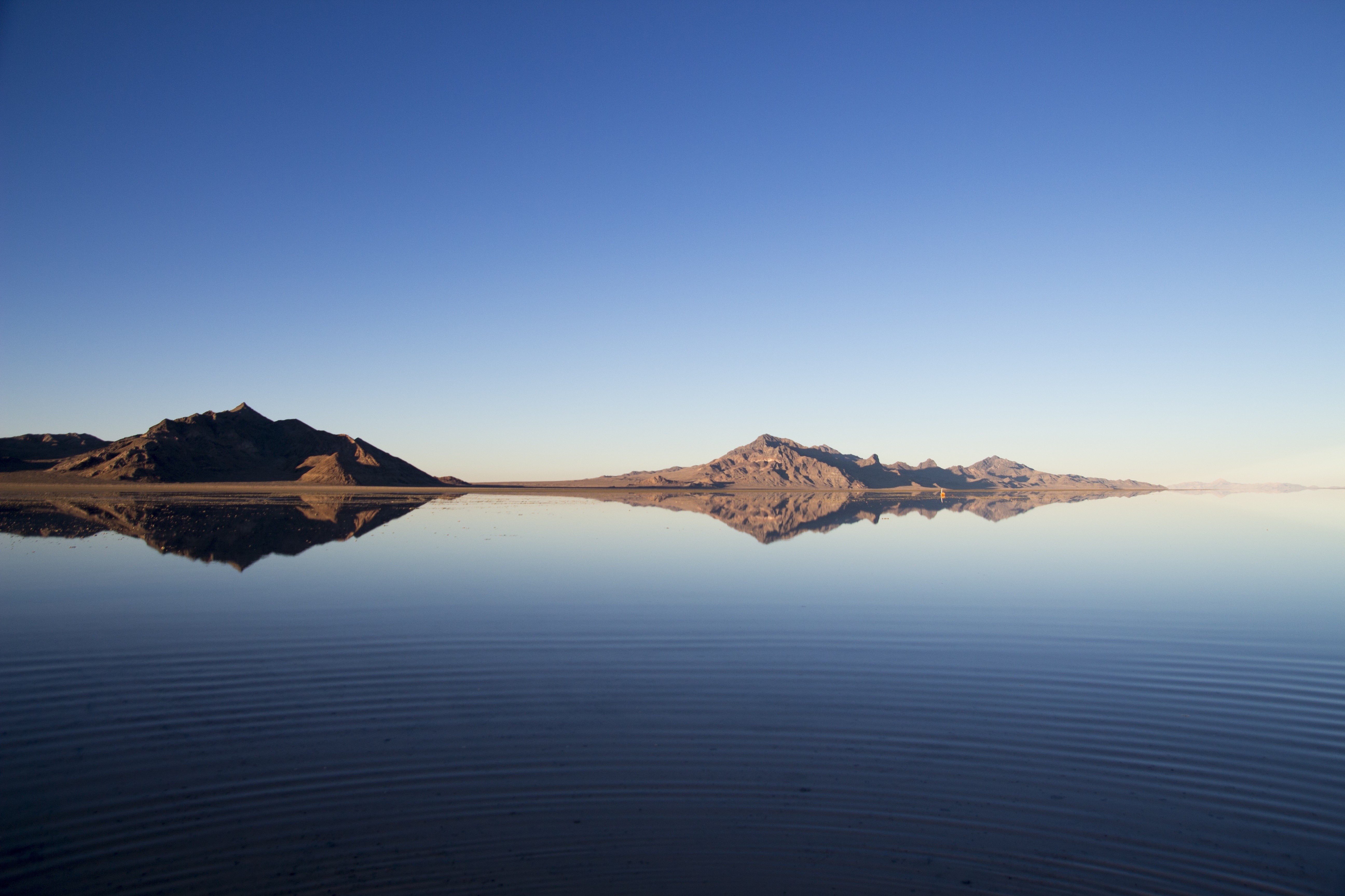 Mountains reflected in a calm body of water under a clear sky HD Wallpaper