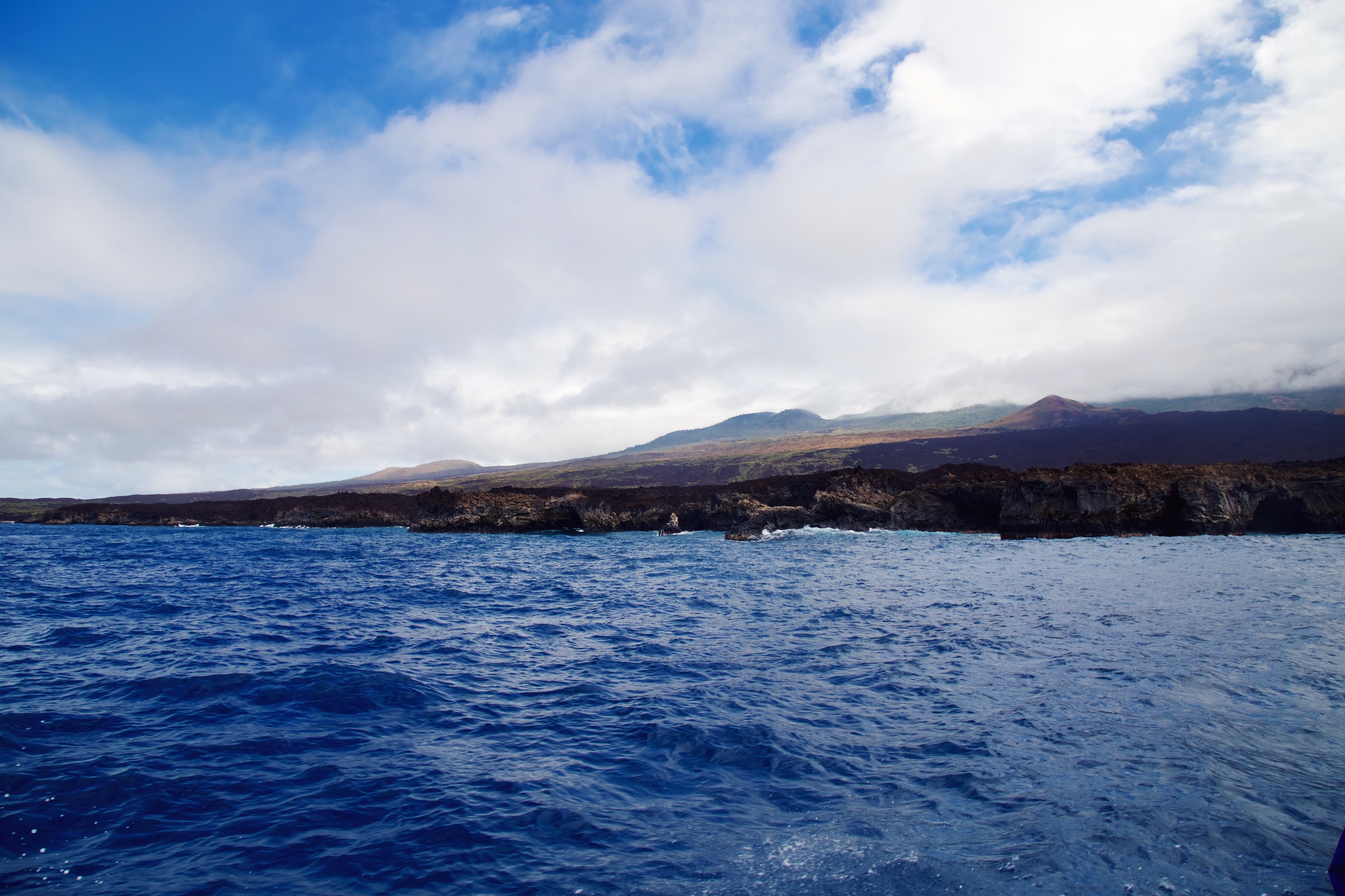 Ocean waves near a rocky coast with mountains under a cloudy sky HD Wallpaper
