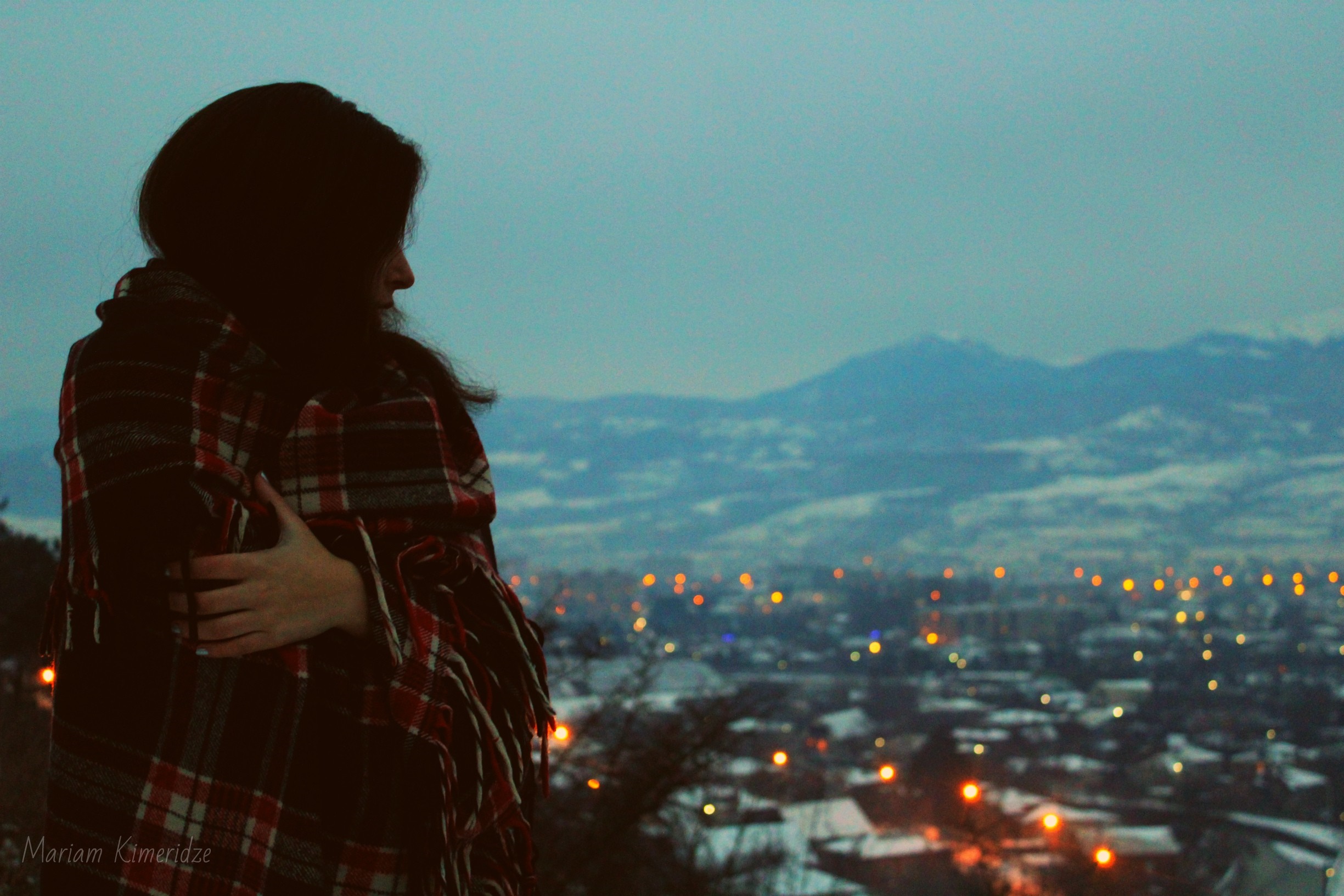 Woman wrapped in a blanket looking at a city at dusk HD Wallpaper