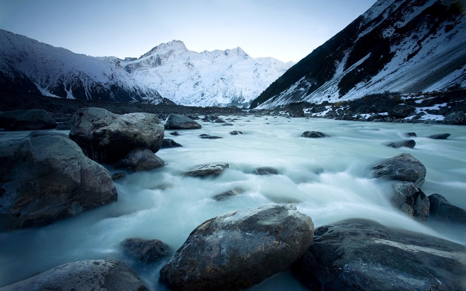 Snow-capped mountains and a glacial river with rocks HD Wallpaper
