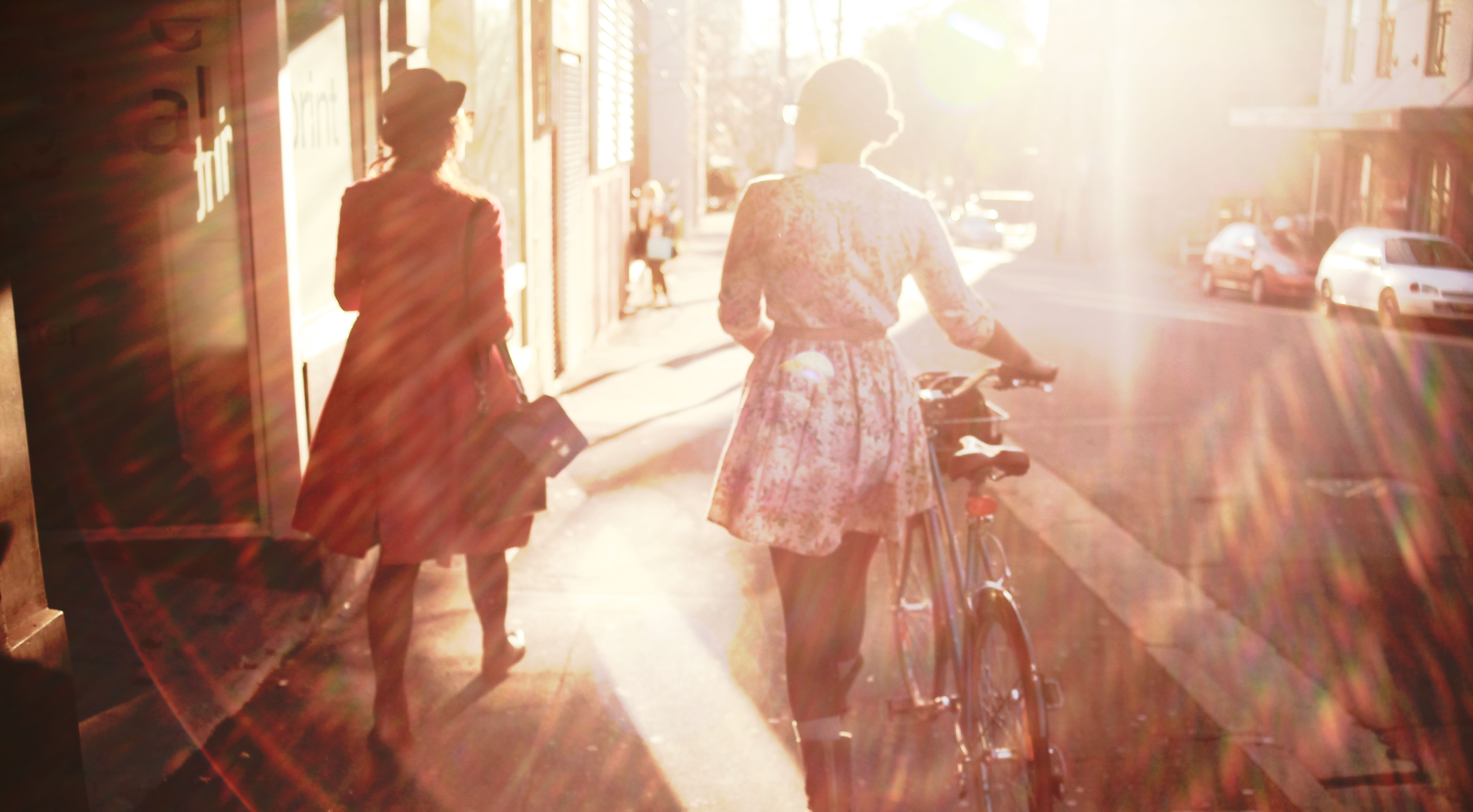 Two women walking with a bicycle in sunlight HD Wallpaper