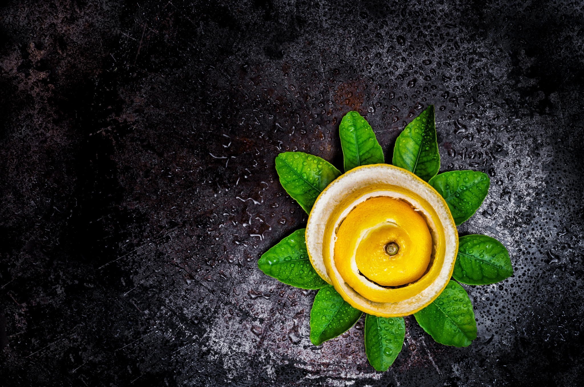 Lemon peel spiral with green leaves on dark surface HD Wallpaper