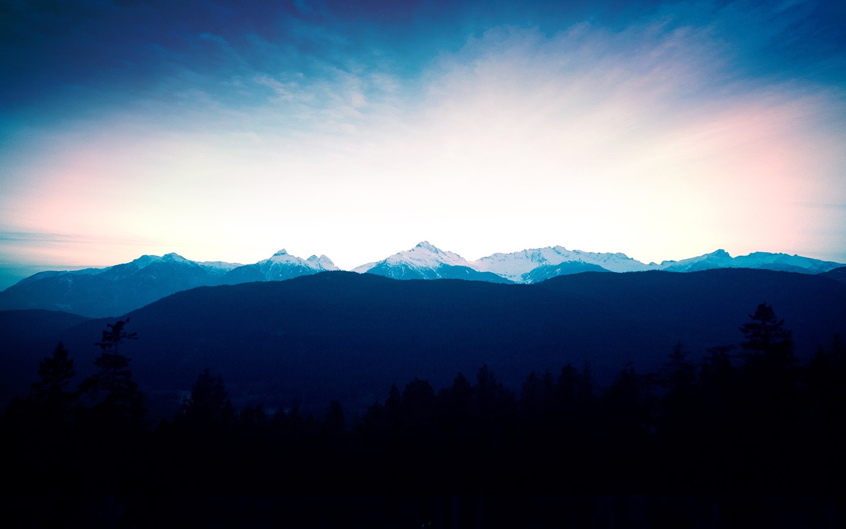 Silhouetted forest in front of snow-capped mountains at sunset HD Wallpaper