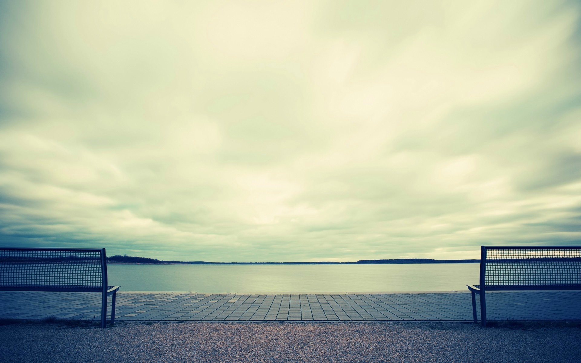 Two empty benches facing a calm lake under a cloudy sky HD Wallpaper