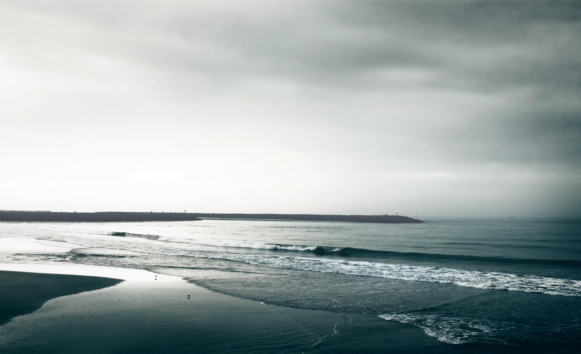 Ocean waves crash on a sandy beach under a cloudy sky HD Wallpaper