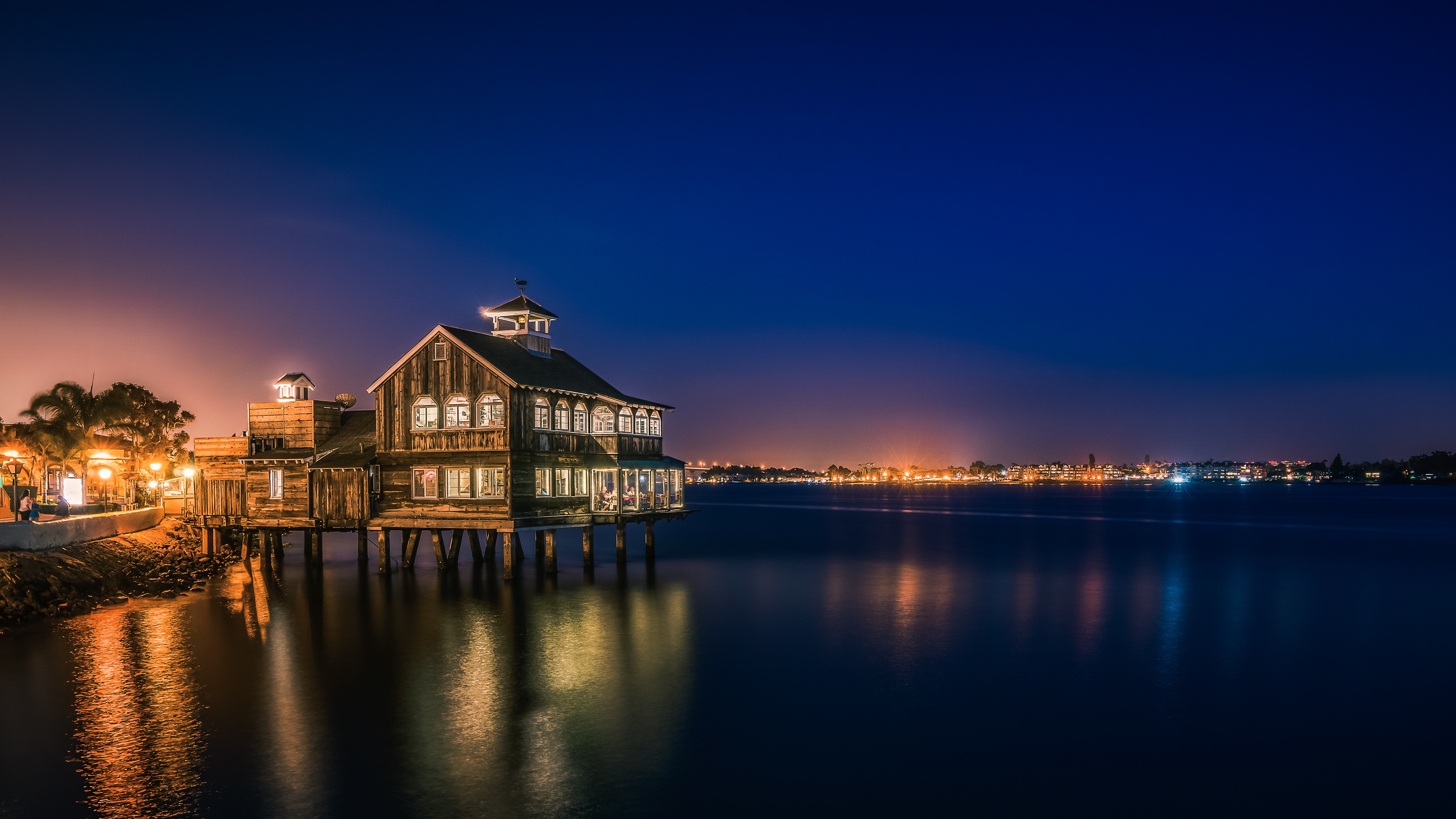 Pier Cafe at night with city lights on the horizon HD Wallpaper