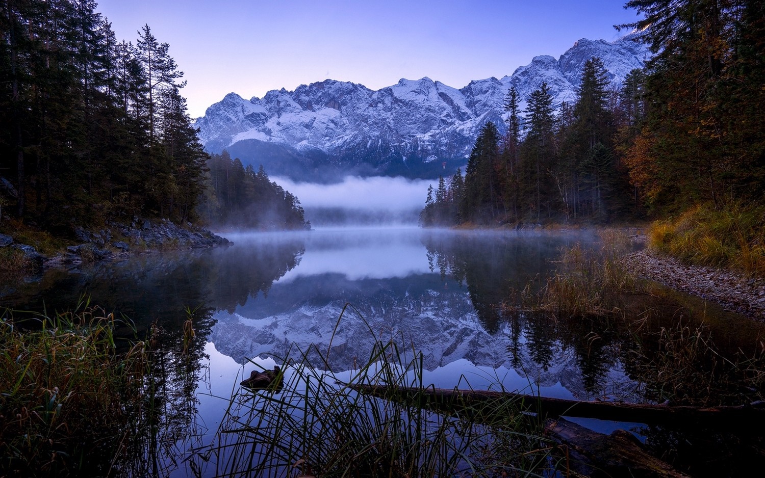 Misty lake reflecting snow-capped mountains and pine forest HD Wallpaper