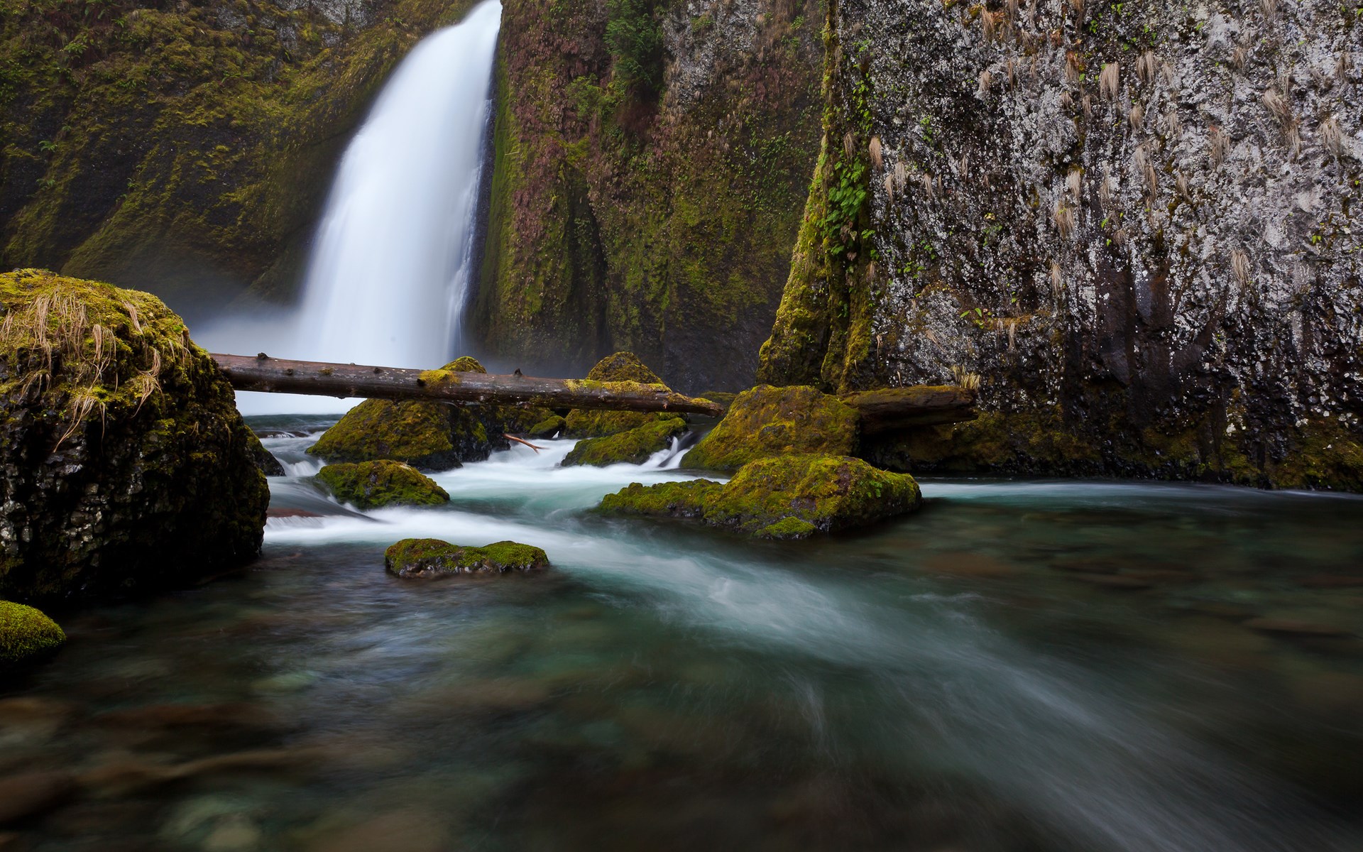 Waterfall flowing over moss-covered rocks into a stream HD Wallpaper