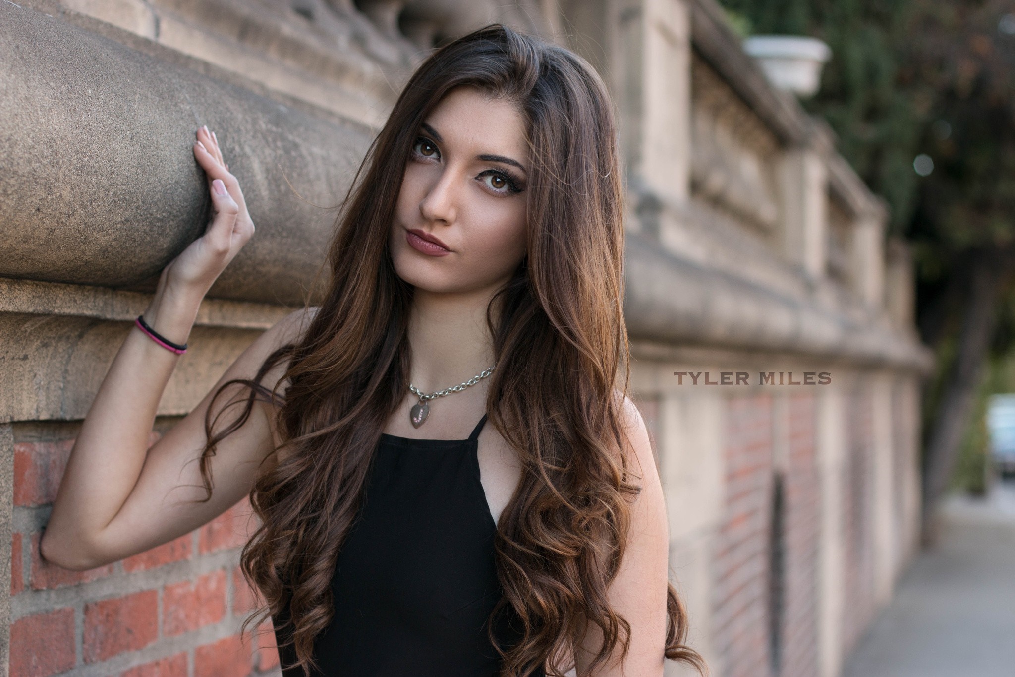 Woman with long brown hair posing by a brick wall HD Wallpaper