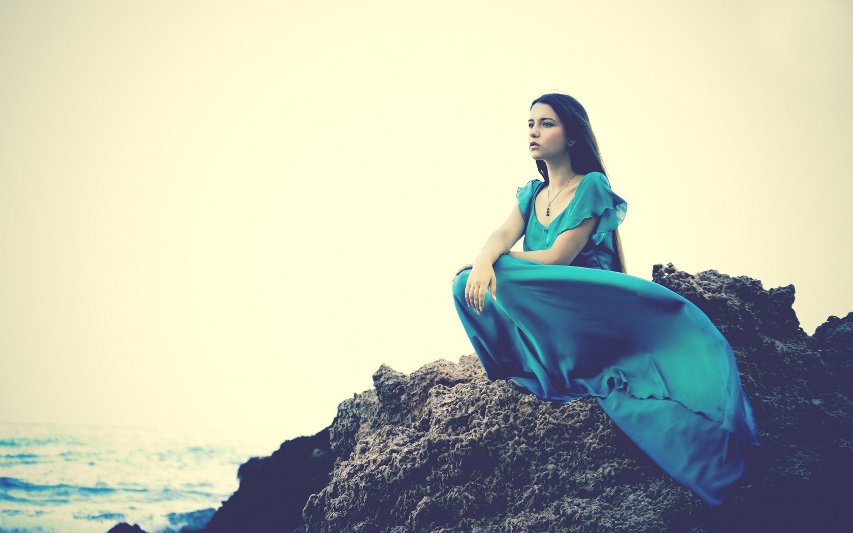 Woman in blue dress sitting on rocks by the sea HD Wallpaper