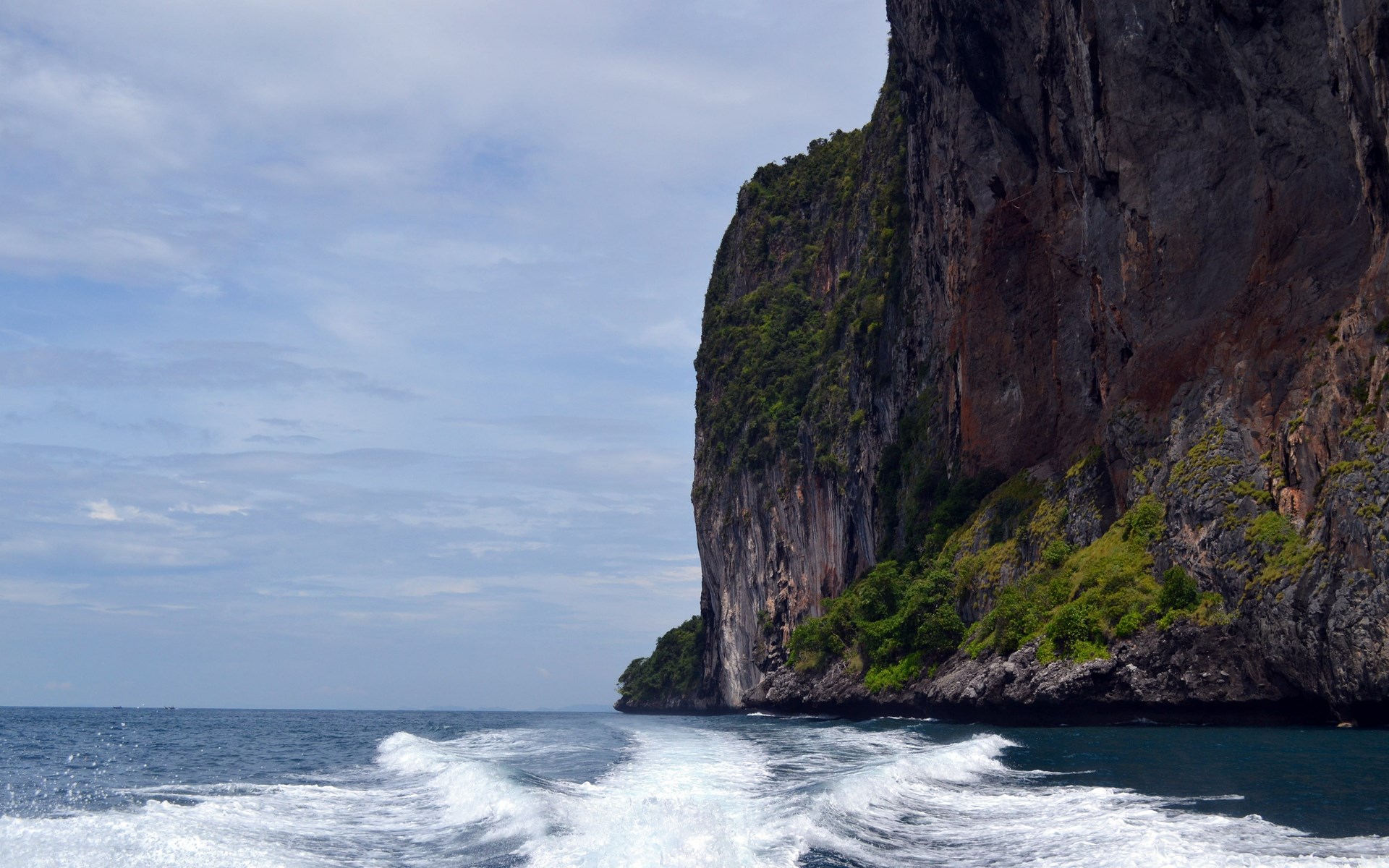 Boat wake near a rocky cliff face in the ocean HD Wallpaper