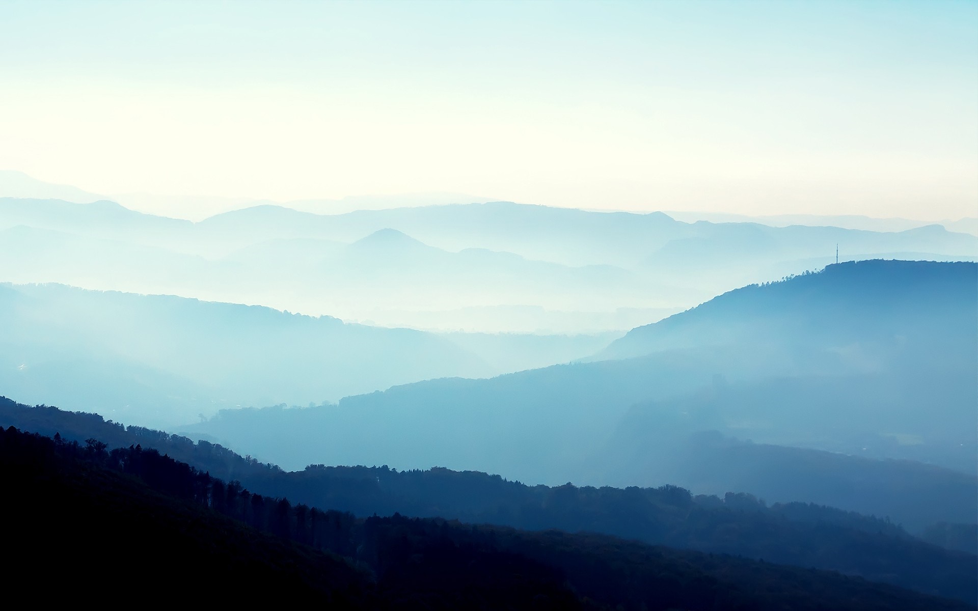Misty mountain range at sunrise with layers of blue hills HD Wallpaper