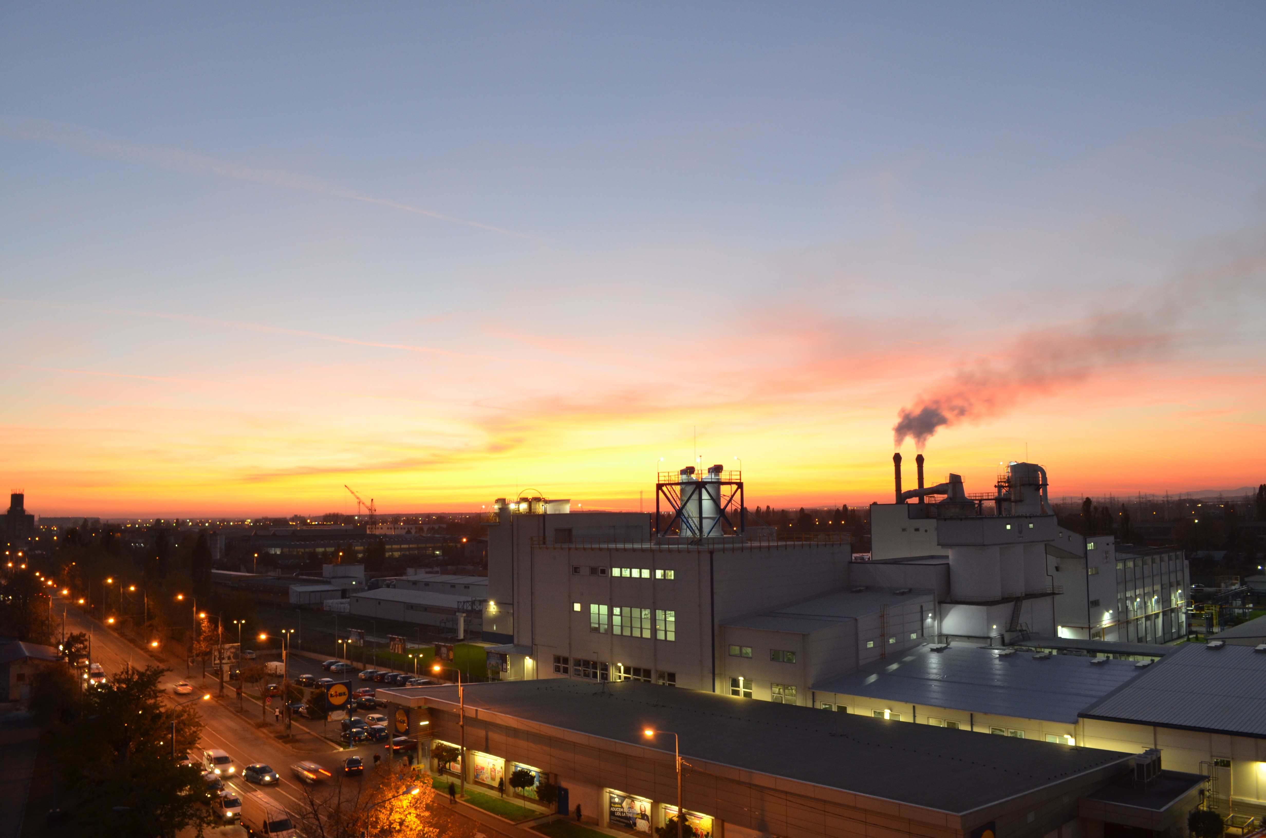 Factory emitting smoke at sunset over a city HD Wallpaper
