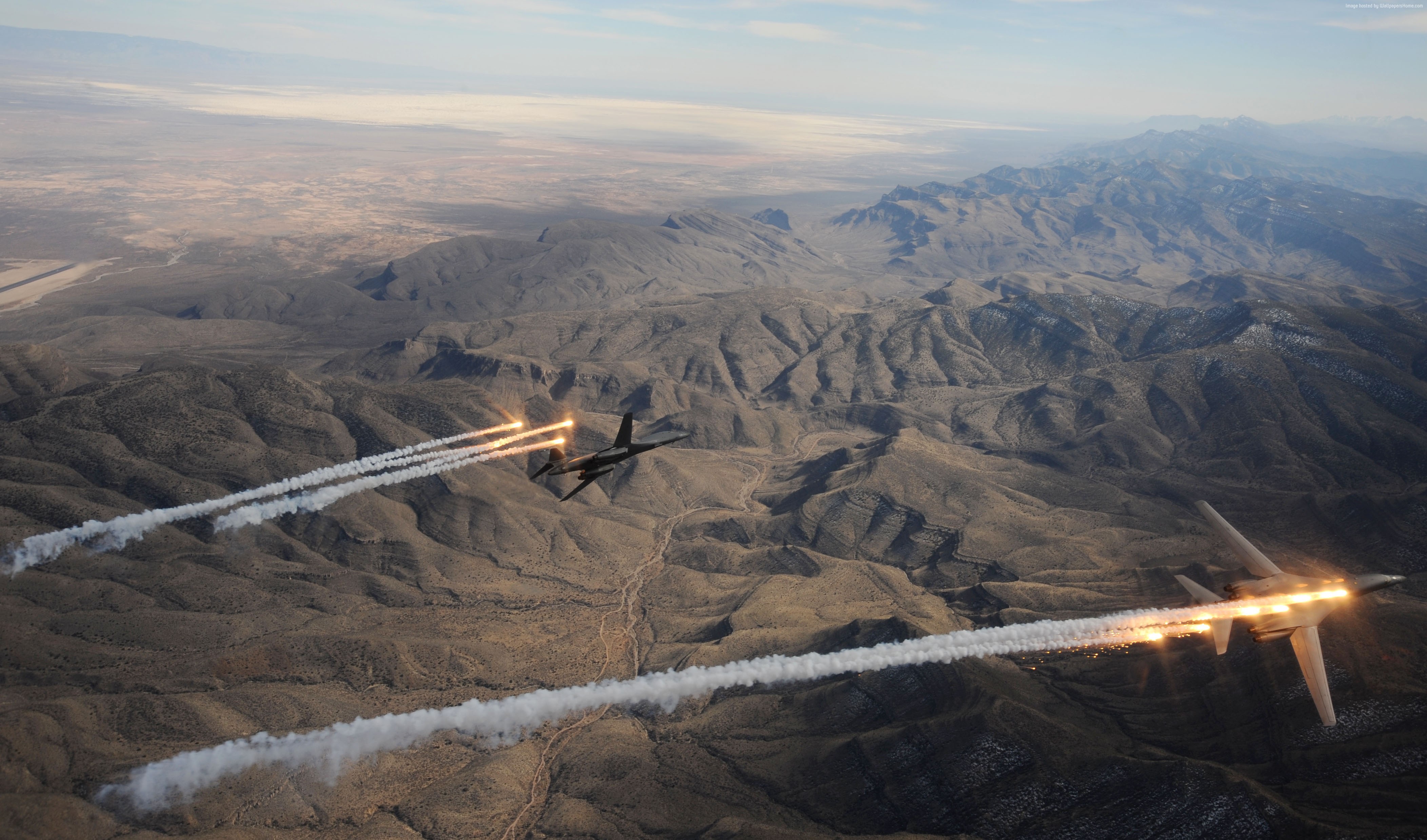 Rockwell B-1 Lancer aircraft releasing flares over mountains HD Wallpaper