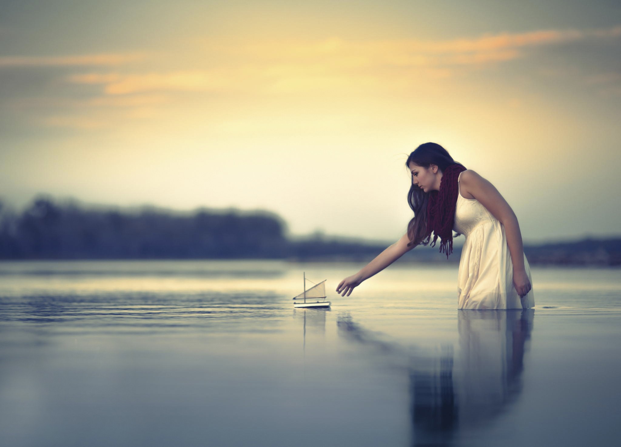 Woman in white dress touching toy boat in water at sunset HD Wallpaper