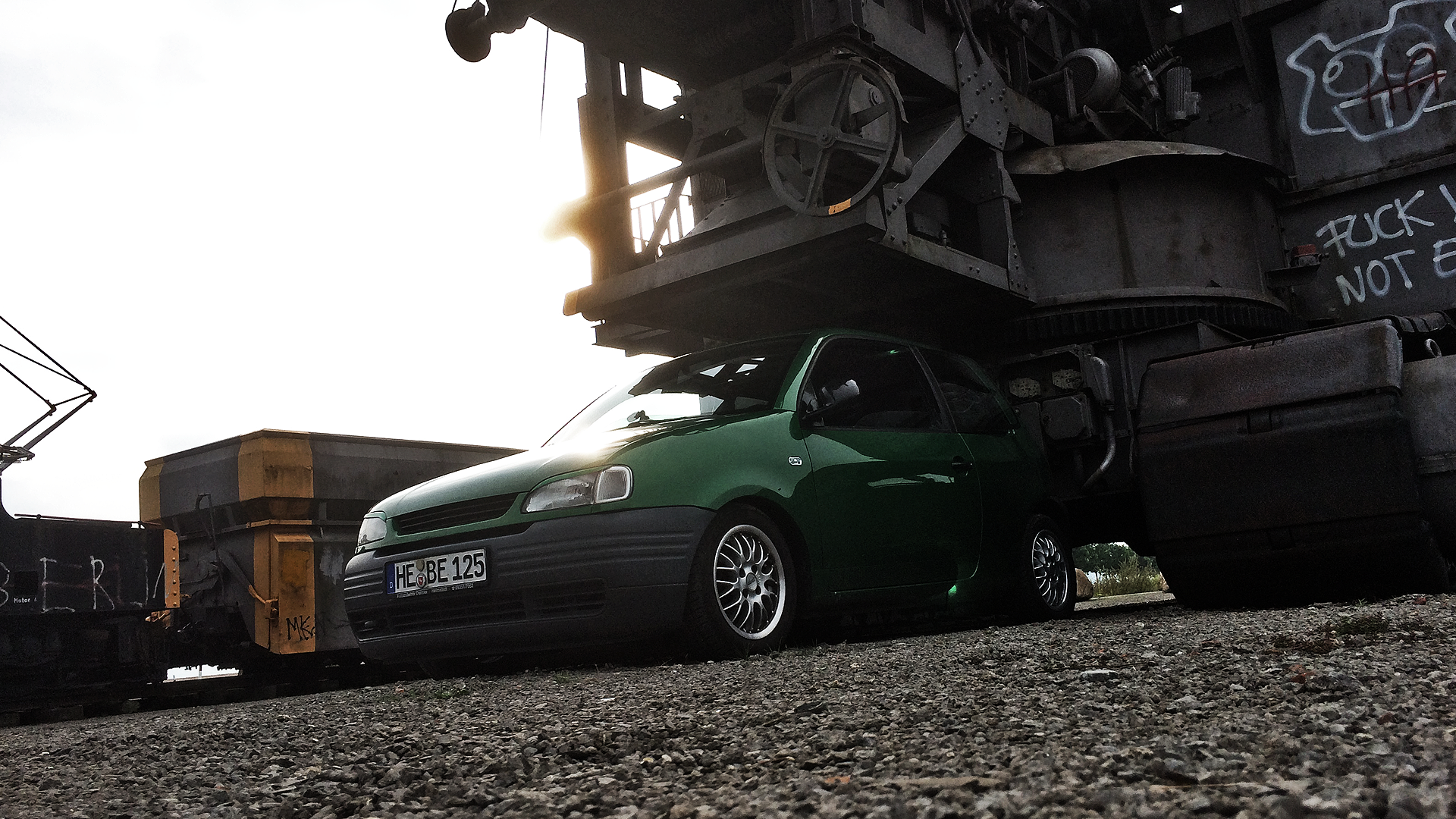Green Volkswagen Seat Arosa parked near industrial machinery HD Wallpaper
