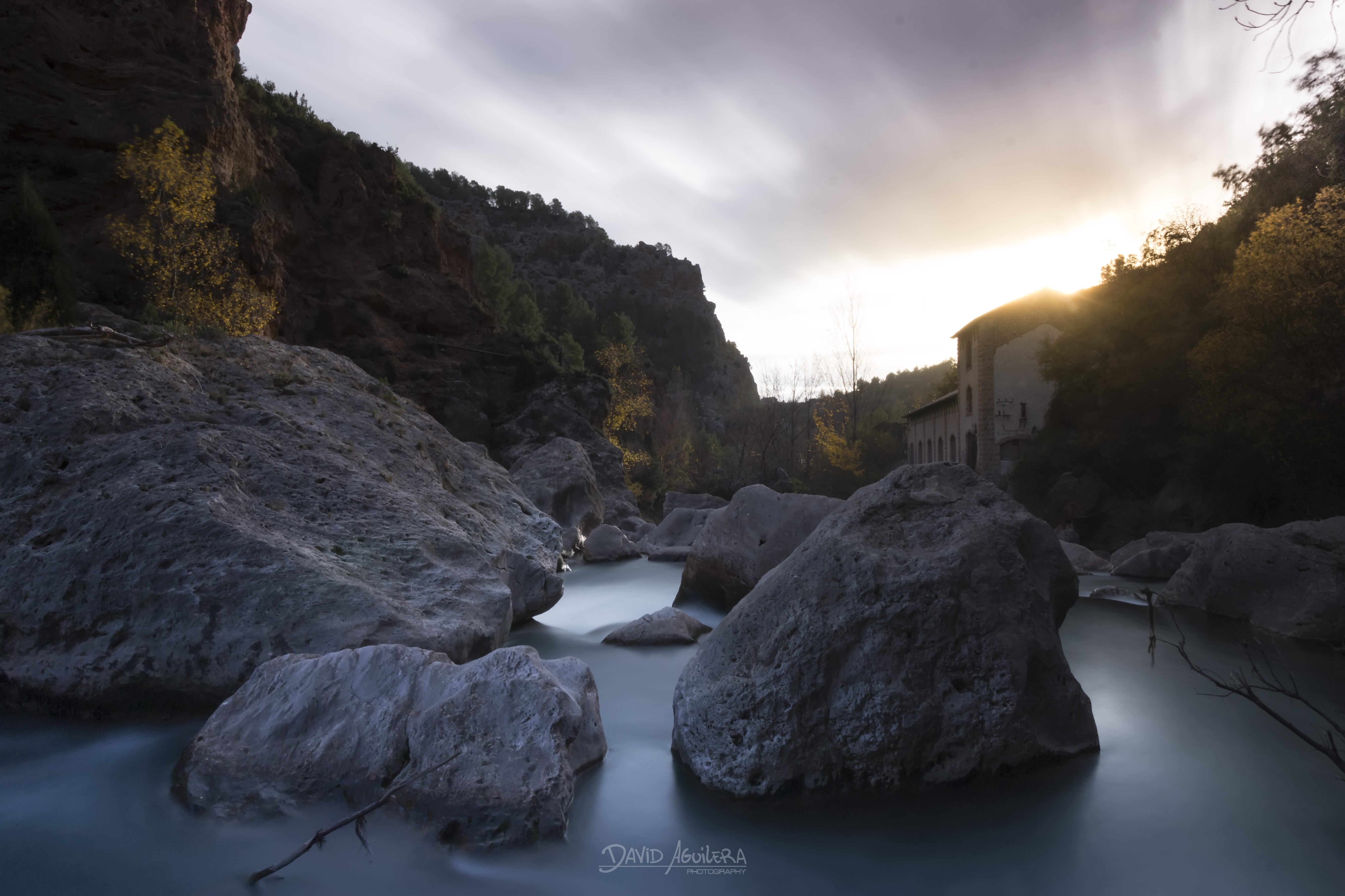 River flowing through rocks with a building at sunset HD Wallpaper
