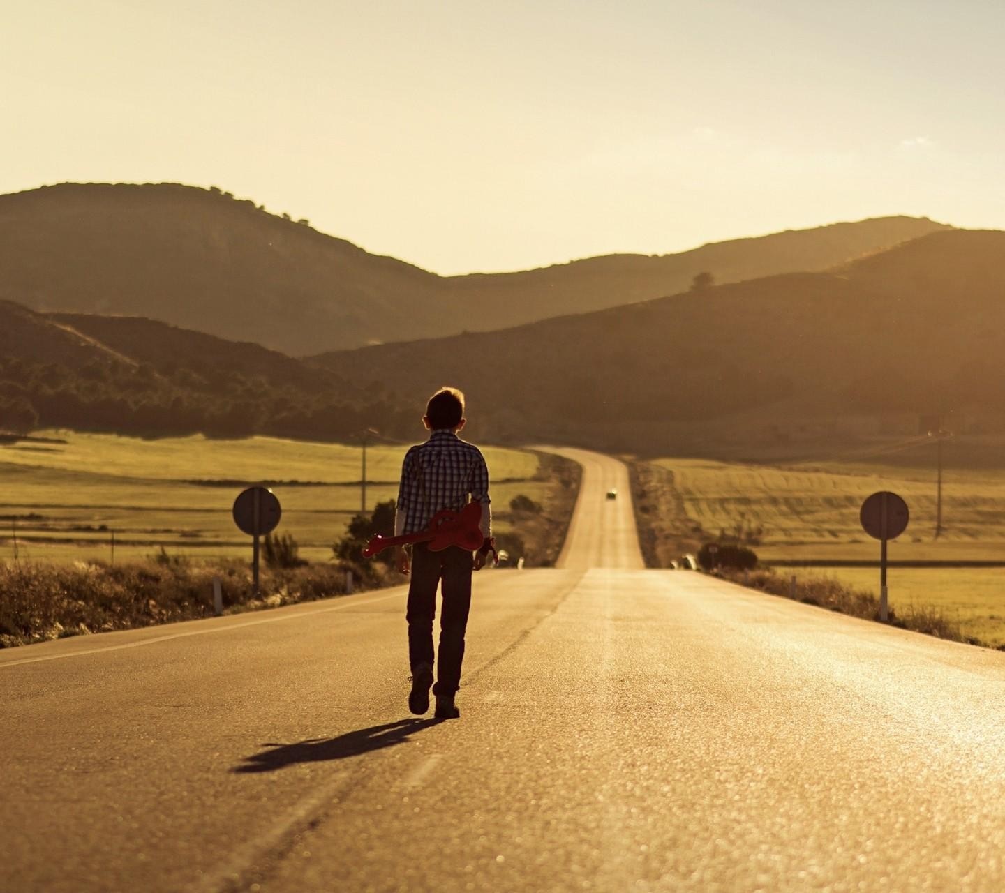 Boy with guitar walking on a road at sunset HD Wallpaper