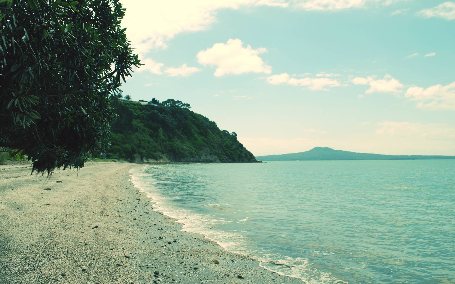 Beach with green hill and distant island HD Wallpaper