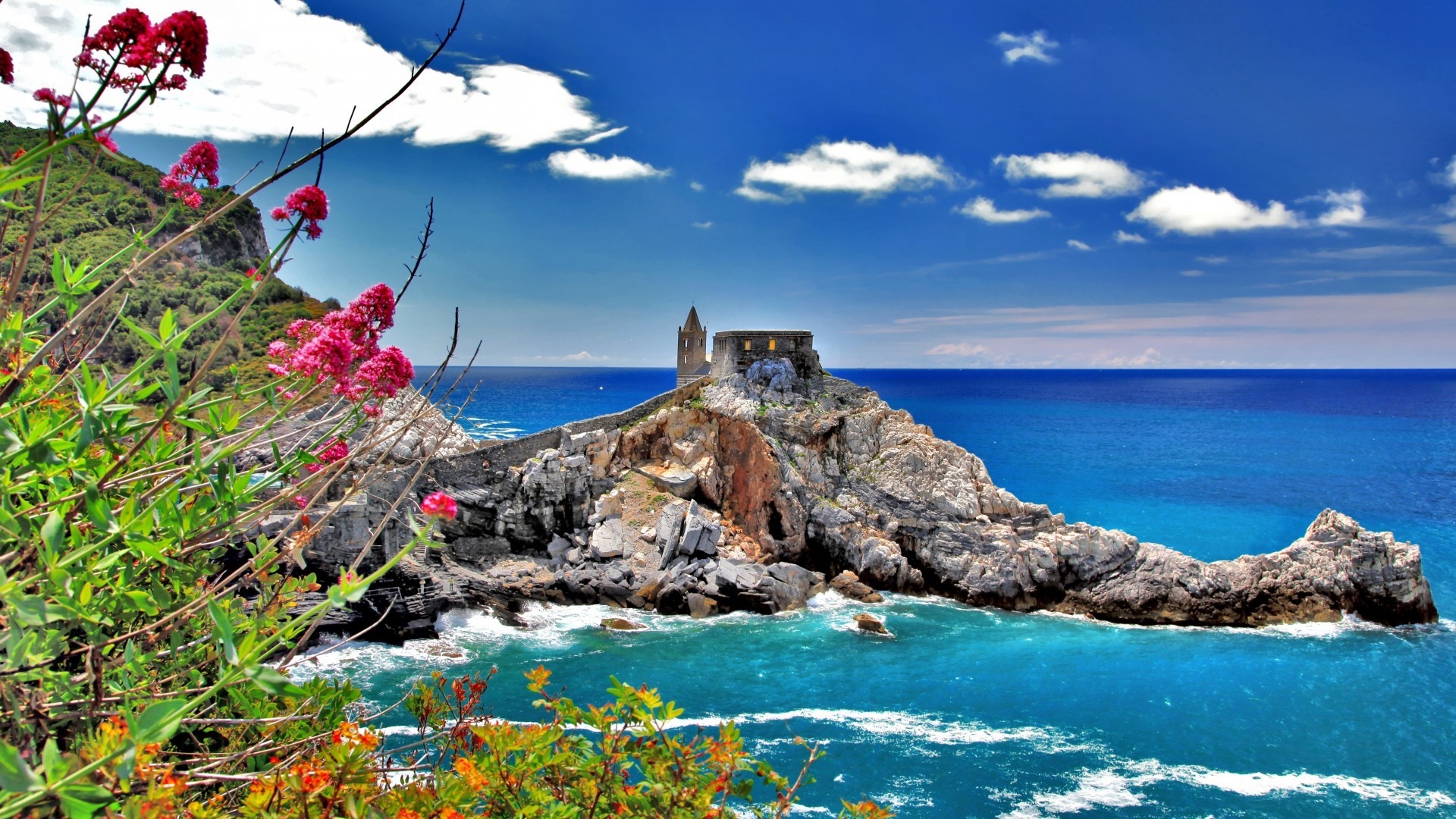 Church on a rocky islet in the sea with flowers in the foreground HD Wallpaper