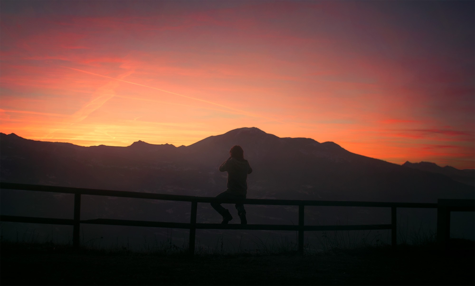 Silhouette of a person sitting on a fence at sunset HD Wallpaper