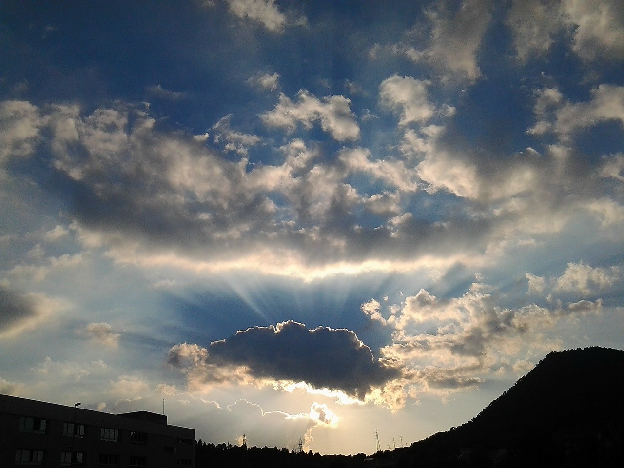 Sunbeams breaking through clouds at sunset over a hill and building HD Wallpaper