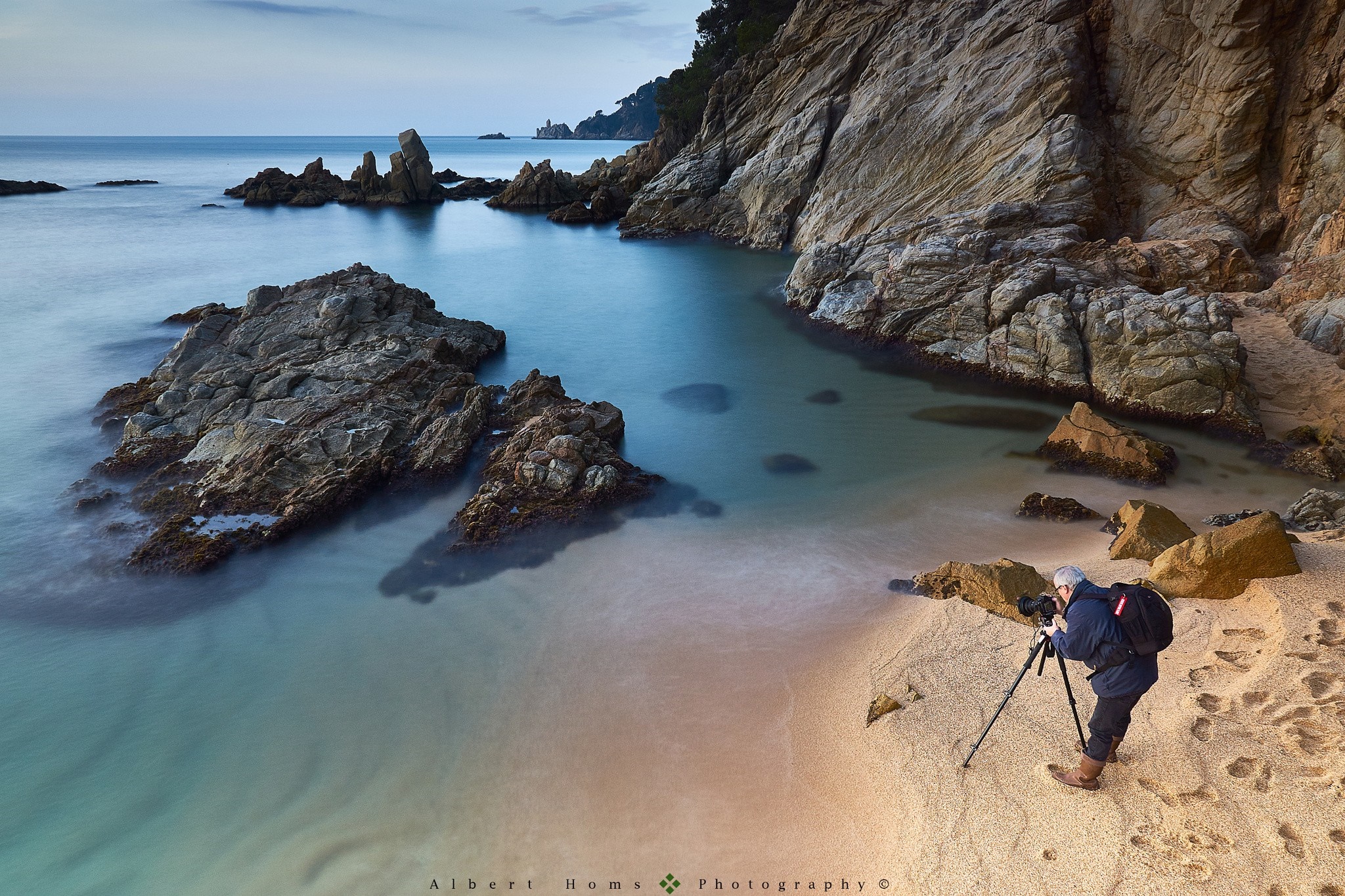 Photographer on a rocky beach with calm sea HD Wallpaper