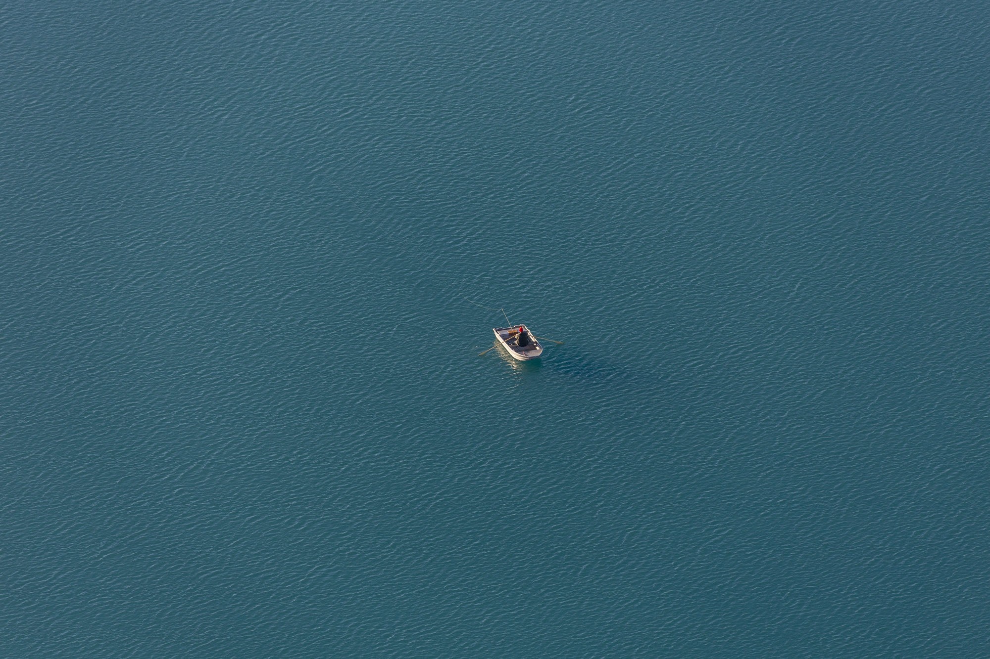 A lone fisherman in a small boat on a vast blue lake HD Wallpaper