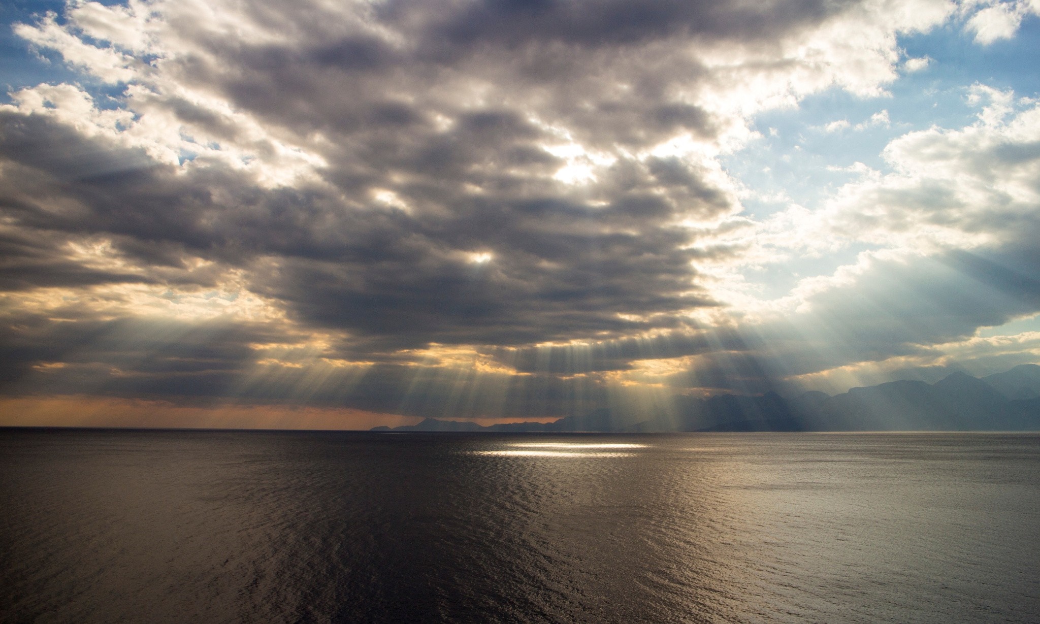 Sunbeams breaking through clouds over the sea at sunset HD Wallpaper