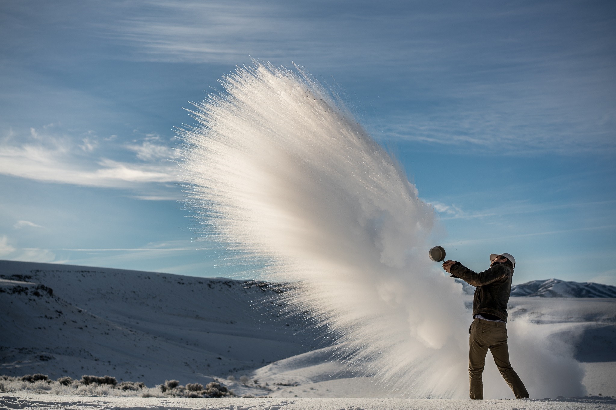 Man throwing hot water into freezing air in snowy landscape HD Wallpaper