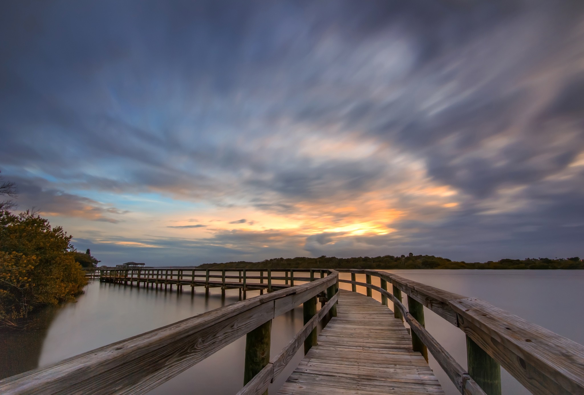 Wooden pier over calm water at sunset with dramatic clouds HD Wallpaper